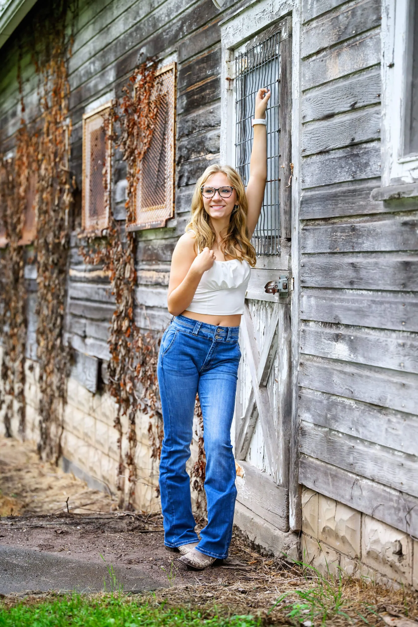 Young woman in a white crop top and flare jeans posing by a weathered barn door.jpg