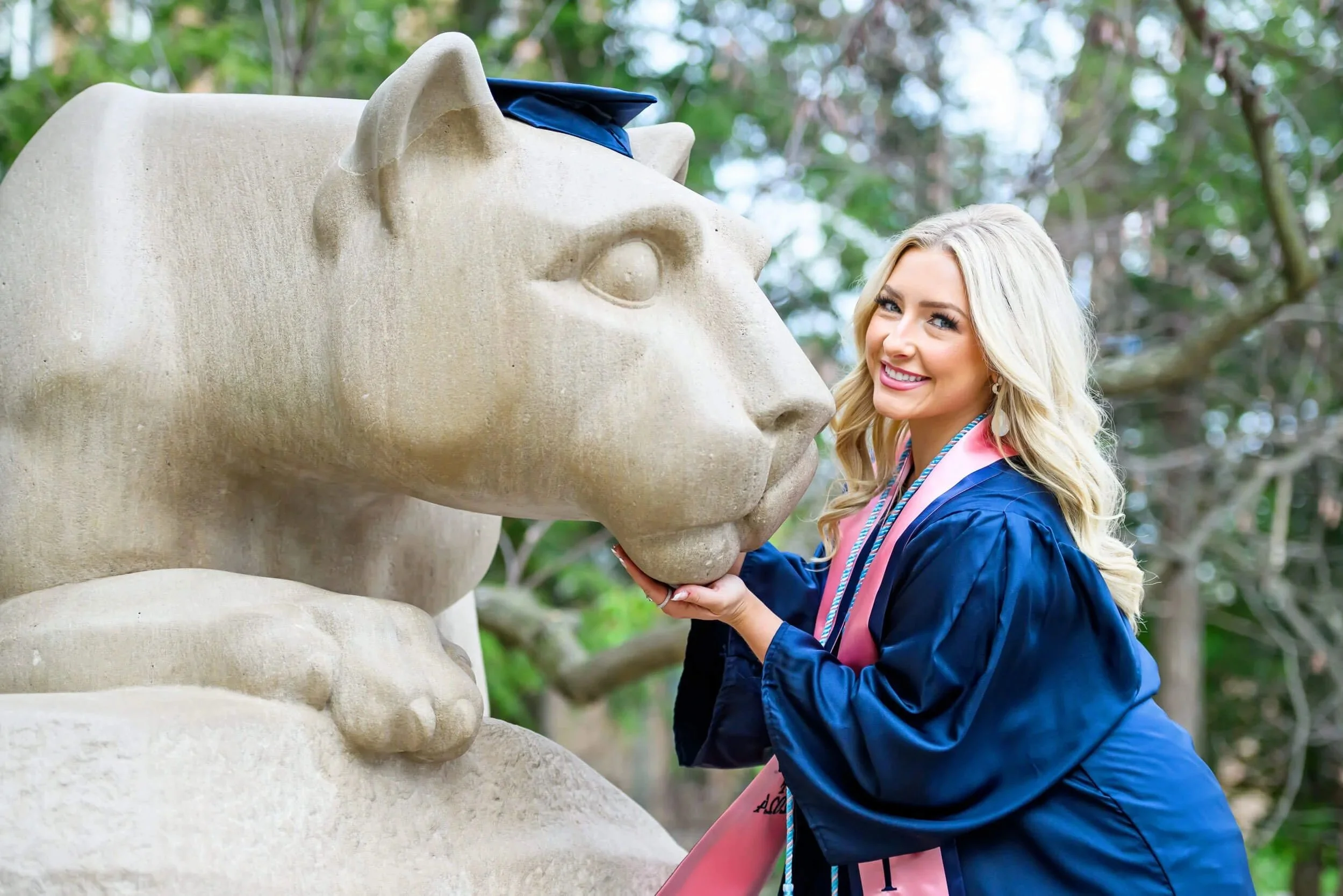 Penn State Grad at Nittany Lion shrine in gown holding Lion and smiling at the camera