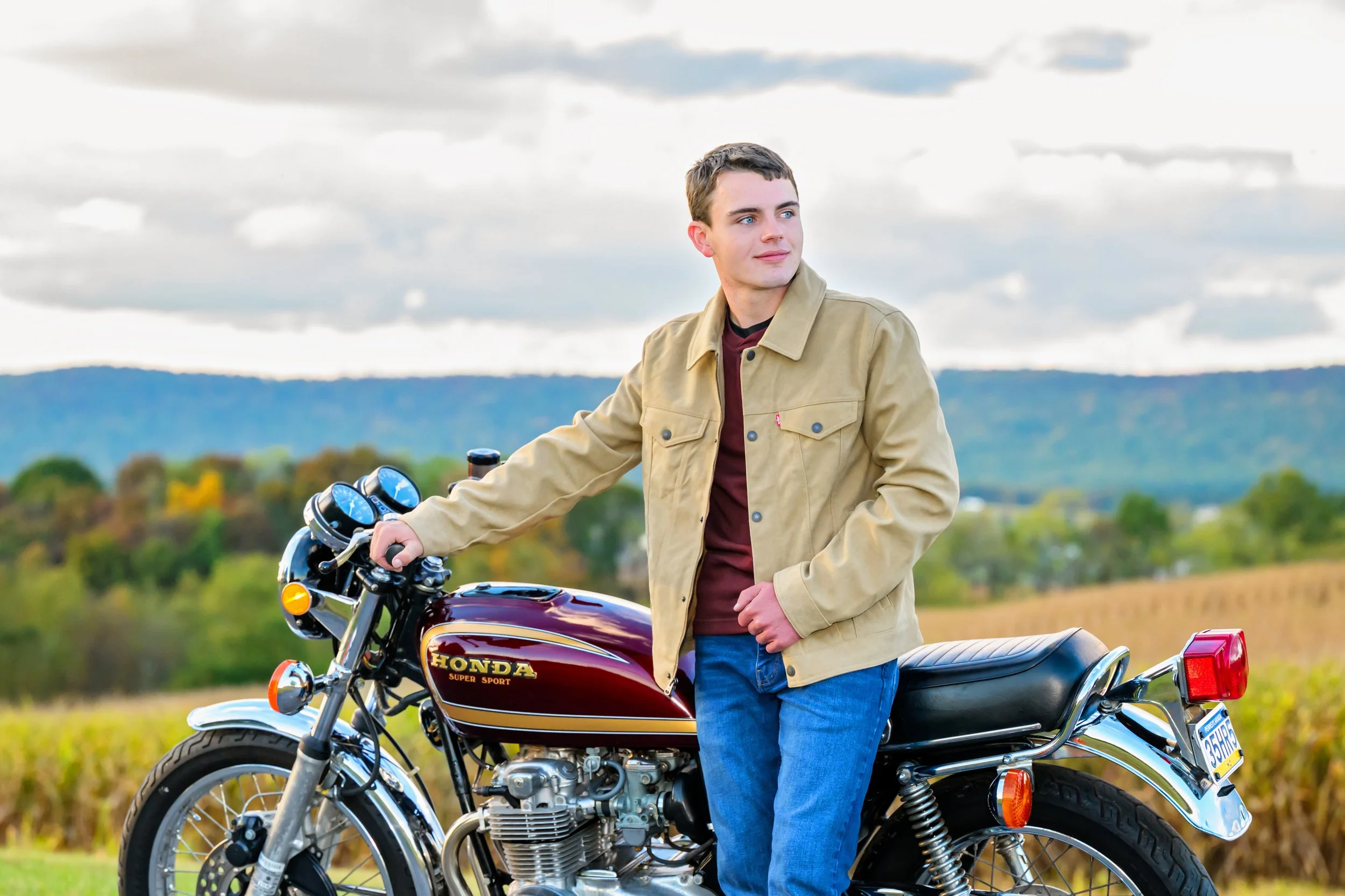 Outdoor senior portrait session of high school senior leaning against his motorcycle with the mountains in the background