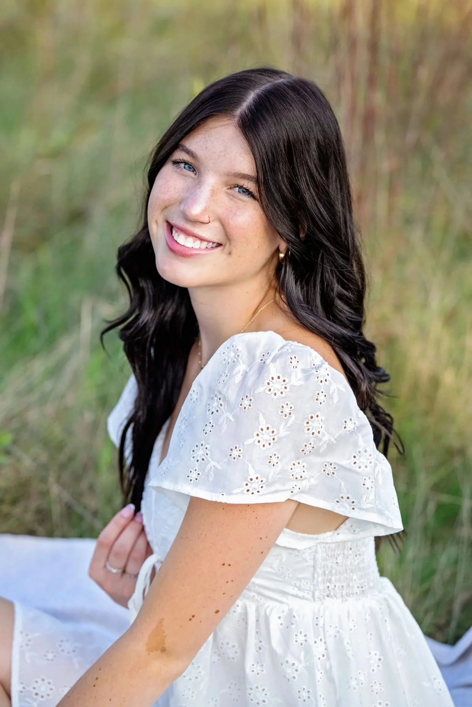 High school senior girl in a white dress sitting in a field during a golden hour portrait session in Williamsport PA