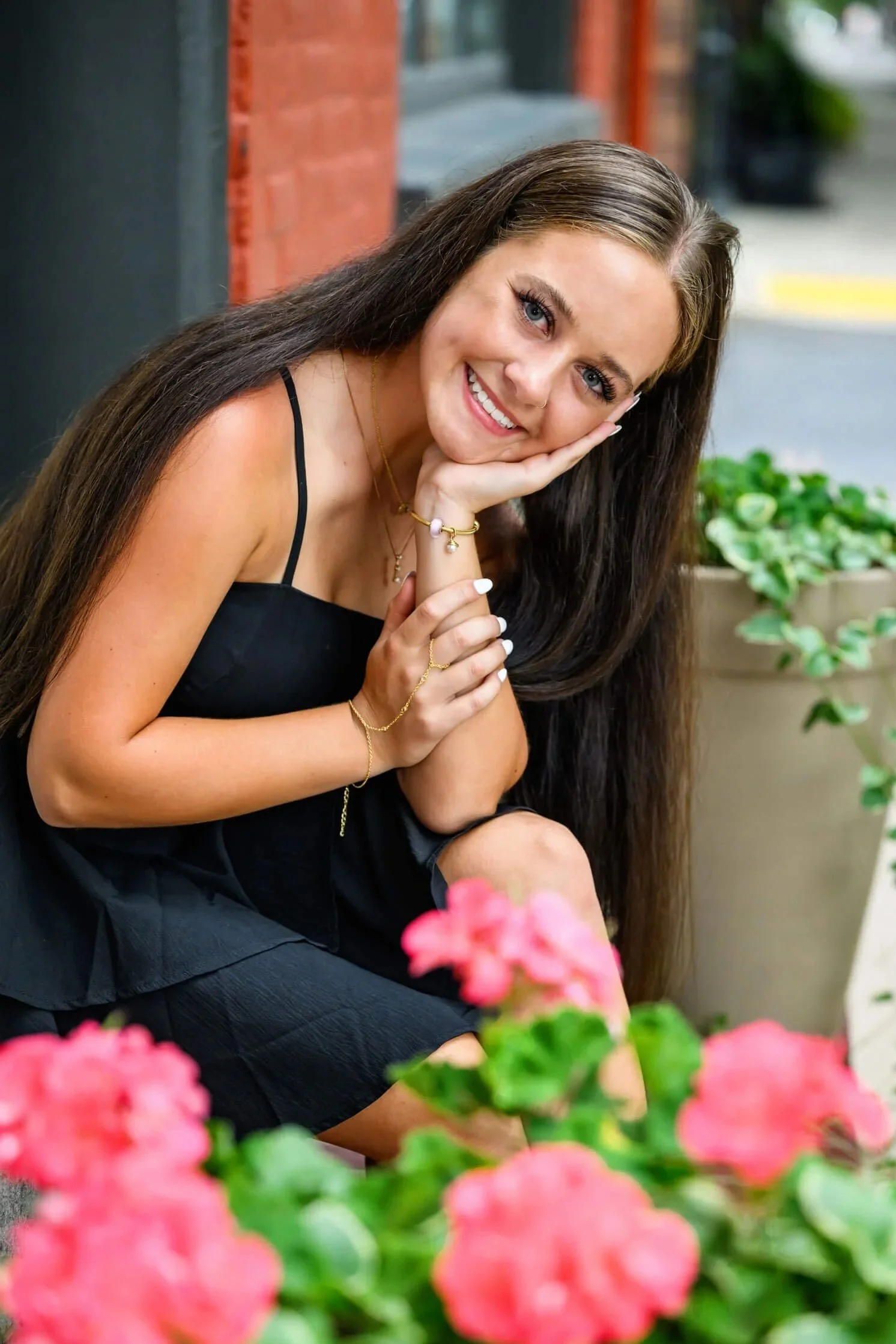 High school senior girl in a black dress sitting on steps in downtown Williamsport Pa by pink flowers