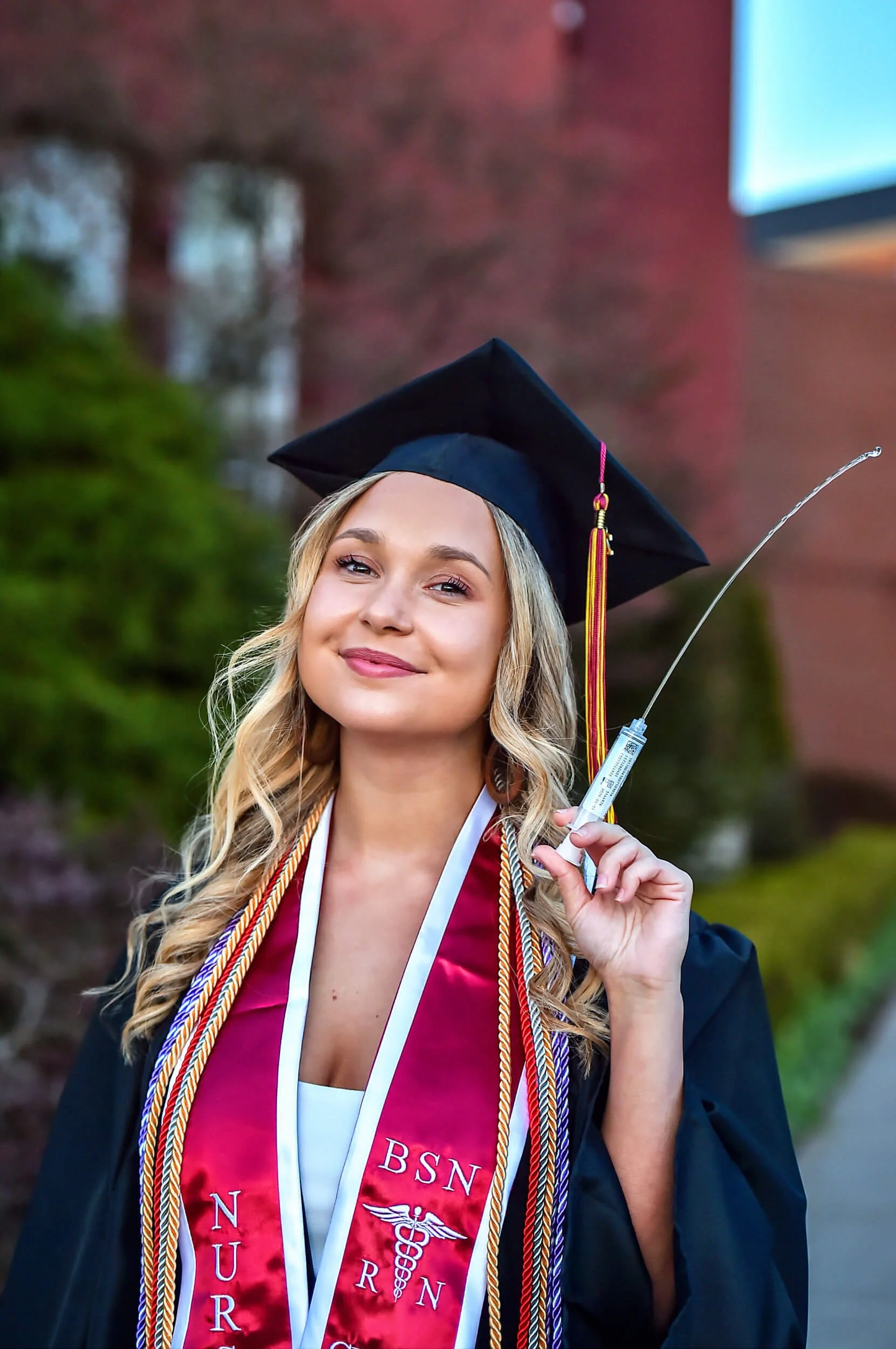 College graduation portrait of a Bloomsburg University graduate in cap and gown holding her nursing syringe during a campus graduation session.