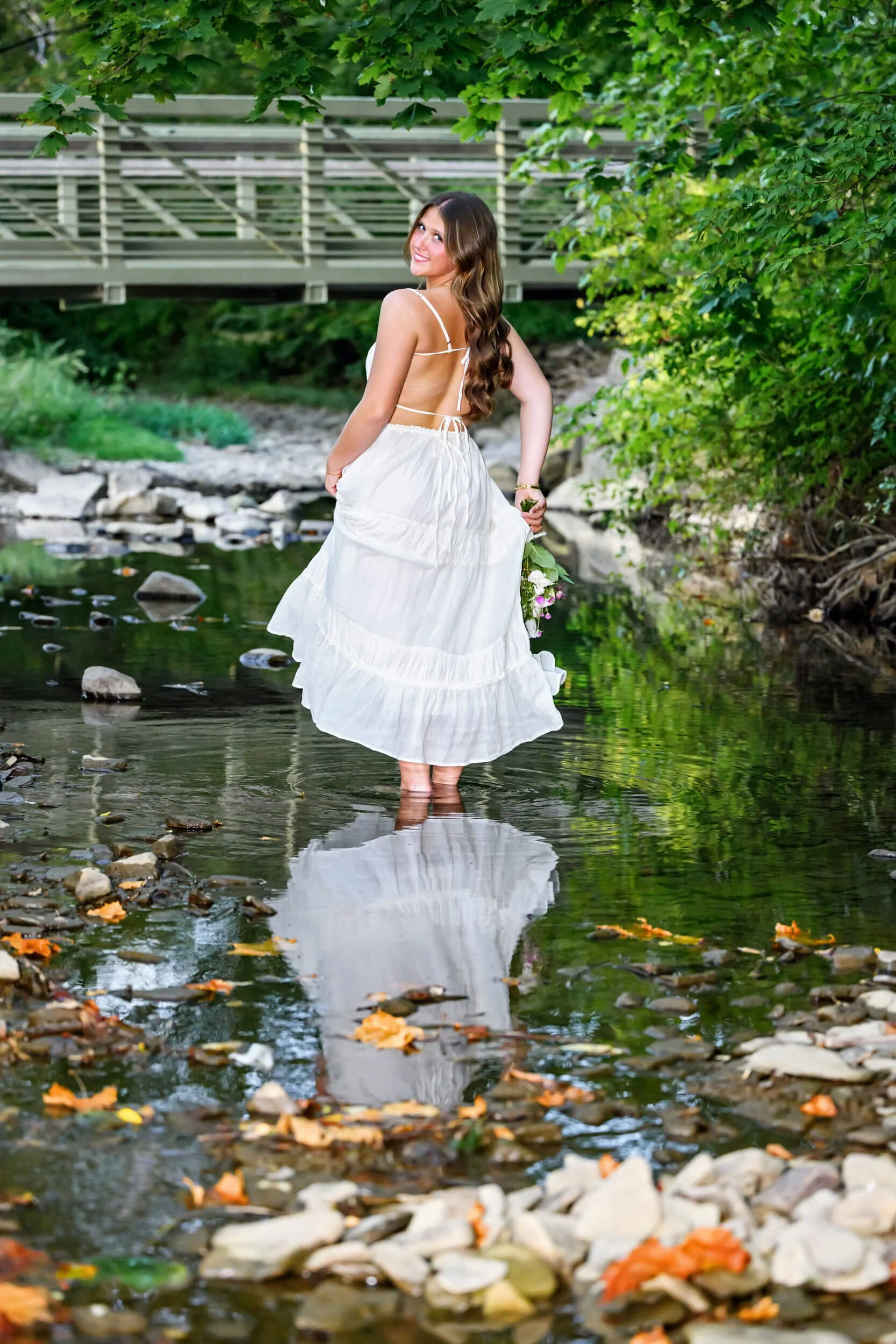 senior photo of high school girl twirling white dress in the creek by a bridge in Williamsport PA