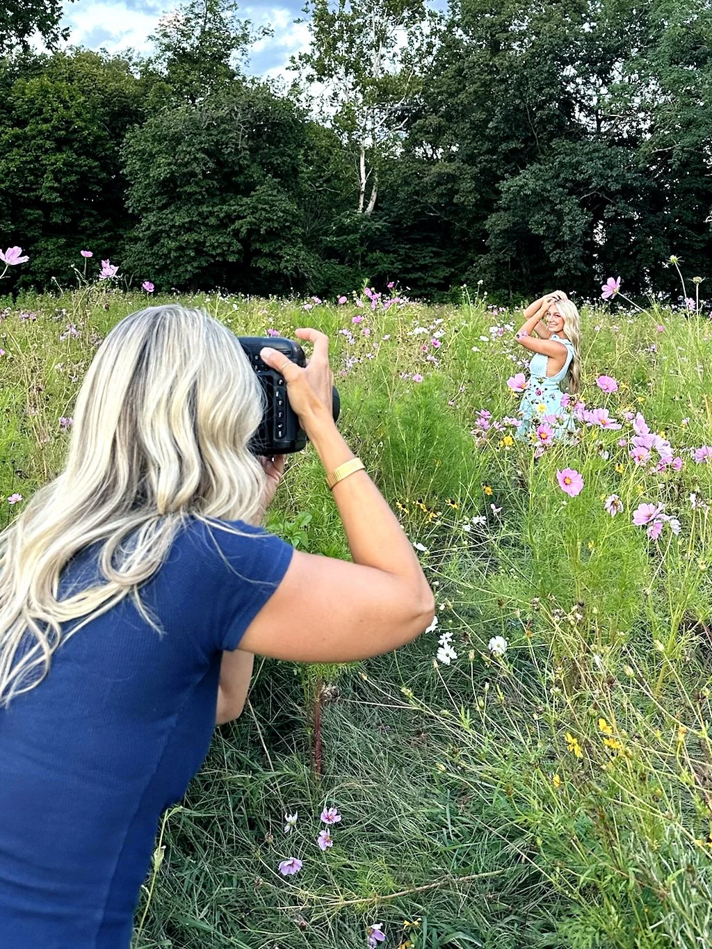 Behind the scenes photo of Tish OConnor taking senior pics of girl in blue dress in wildflower field 