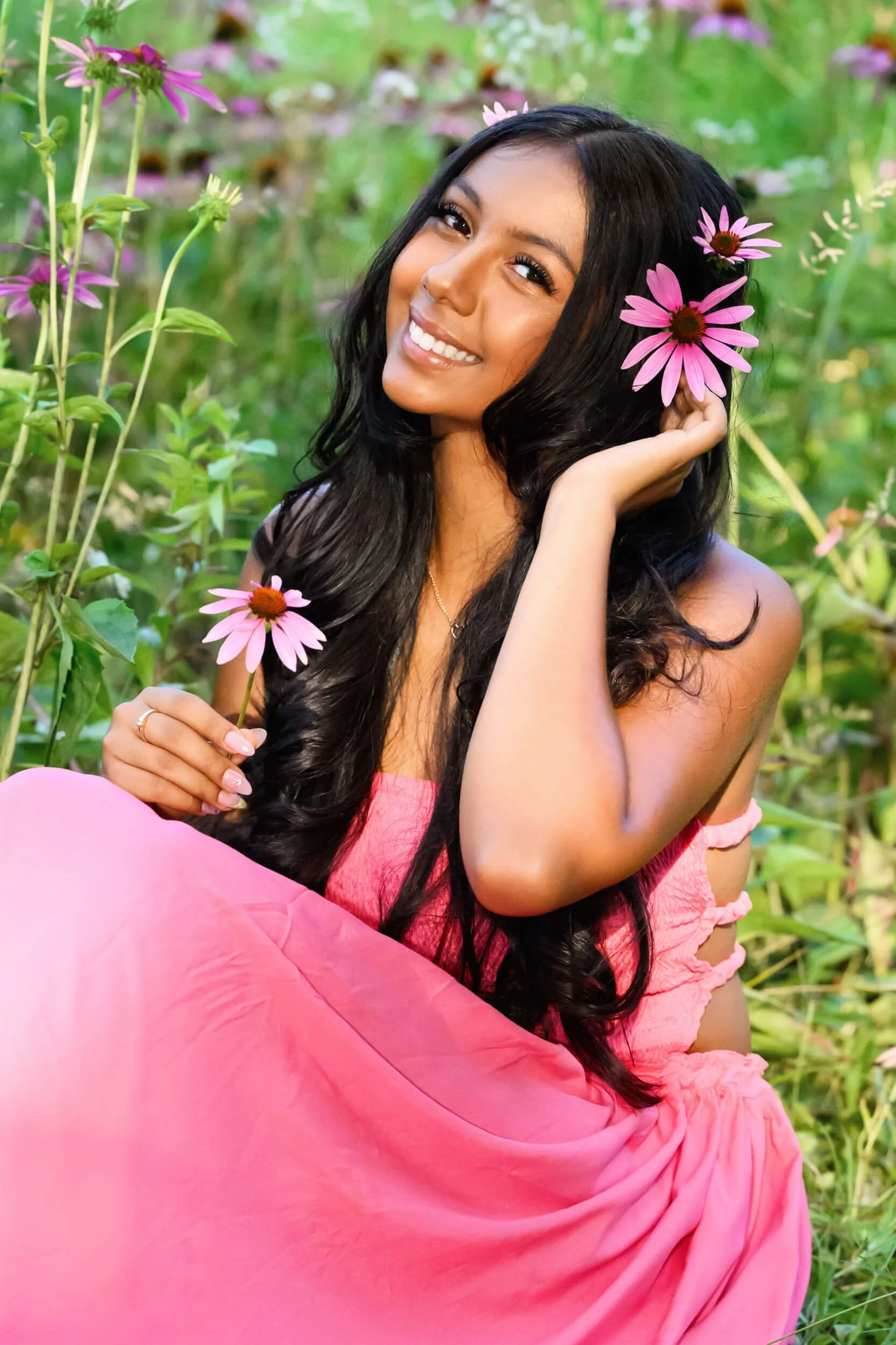 Tish OConnor Photography senior portrait of girl sitting in field with purple coneflowers in pink dress holding flower up to ear