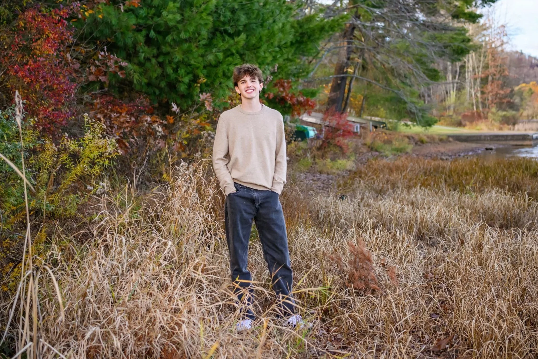 fall senior portrait of guy by lake in golden grass with lots of bright fall colors