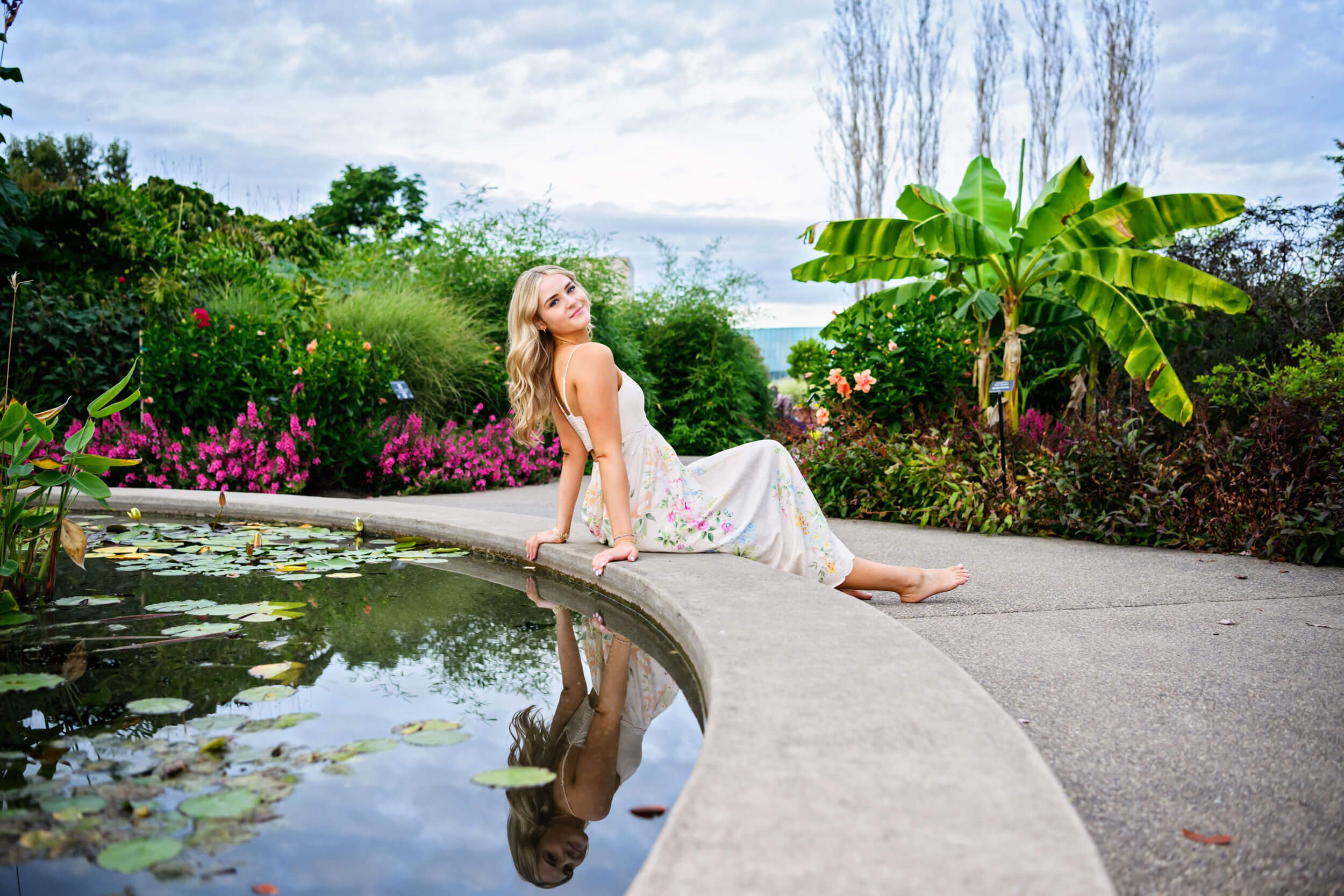 Tish O’Connor, Pennsylvania senior photography portrait session of girls sitting with back to a pond in long pink dress smiling at camera at Penn State Arboretum 