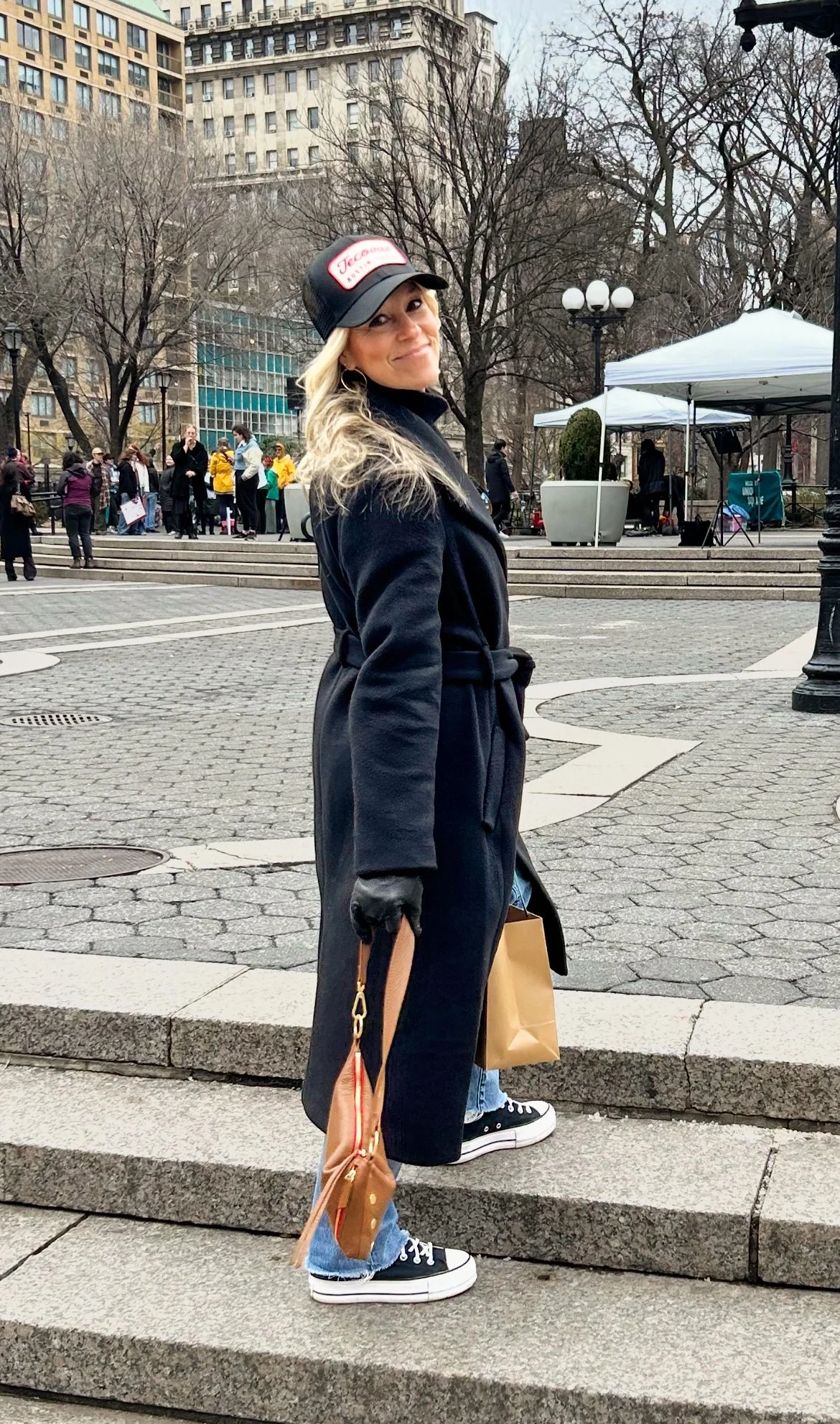 Tish O’Connor, Pennsylvania senior photographer, standing on steps looking back over shoulder  smiling with black long coat and black hat on