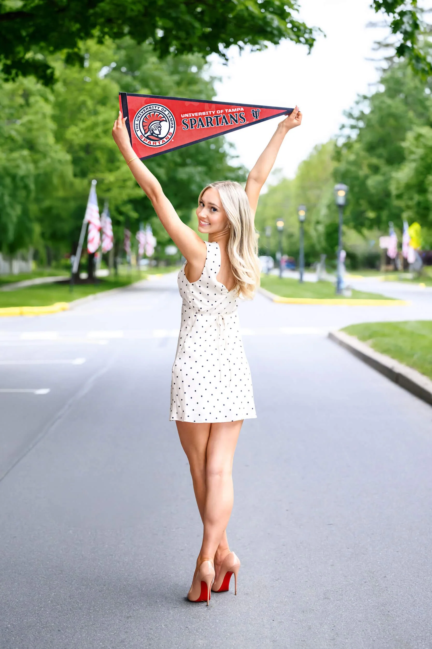 Wellsboro High School senior standing in the street in a polka dot dress holding a collegiate pennant overhead during her senior photo session.
