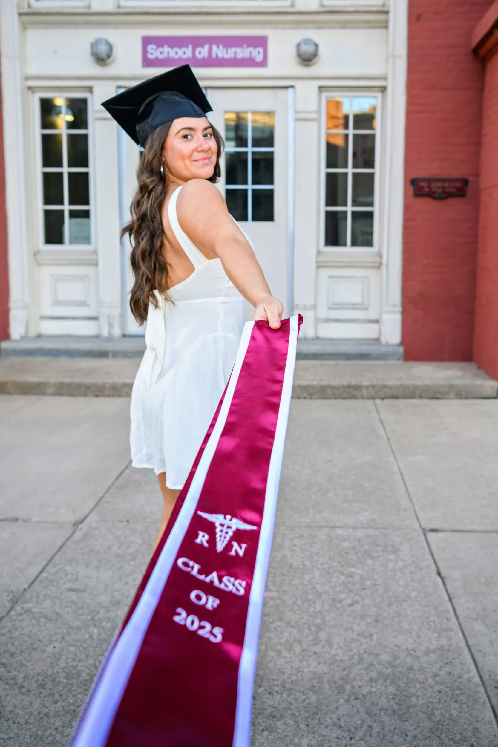 grad portrait of Bloomsburg University graduate looking over shoulder holding stole out in front of school of nursing 