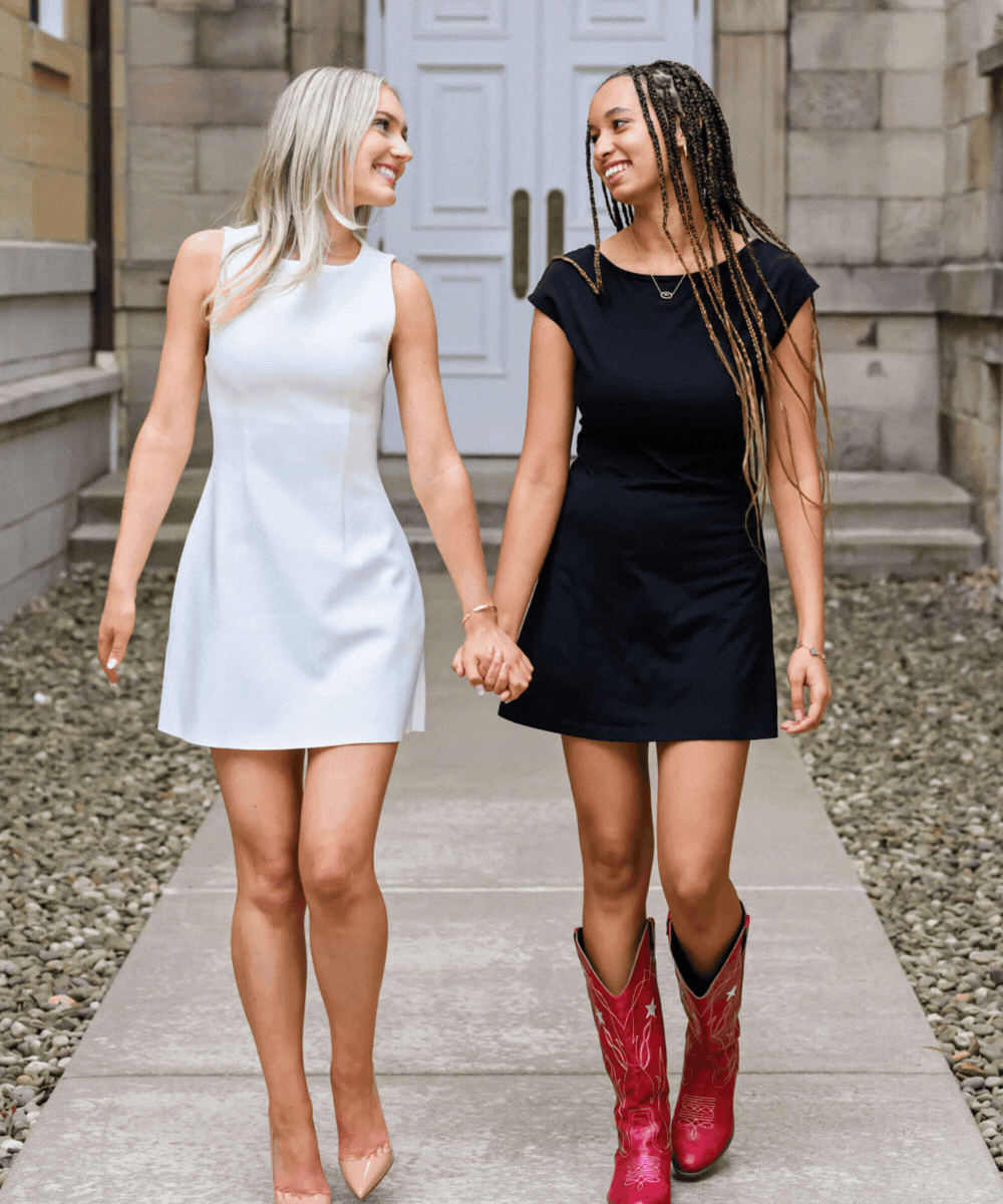 gif of two best friends for senior photos - one in white dress and one in black dress - holding hands walking and looking at eachother 