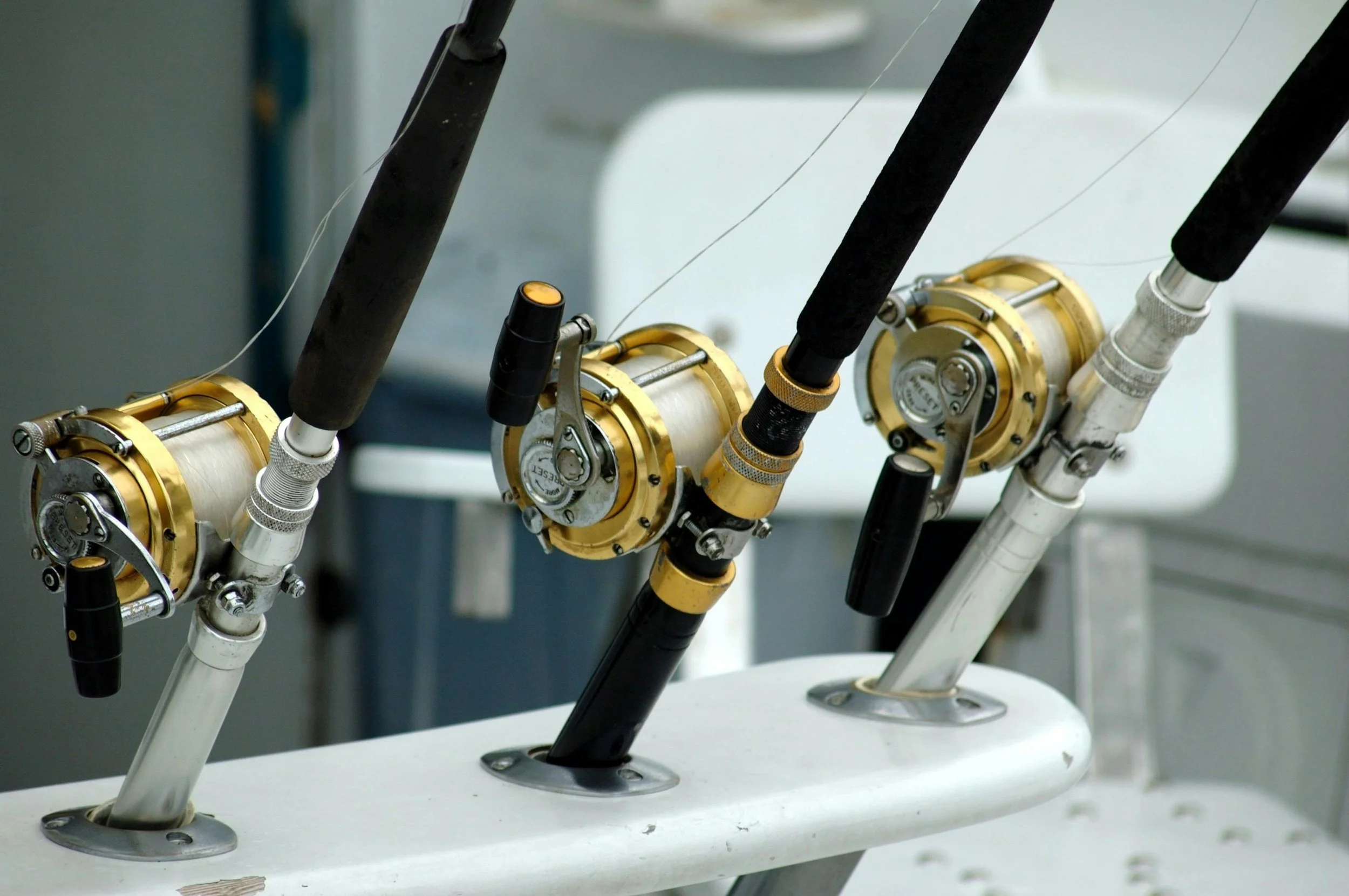 Close-up of fishing reels attached to fishing rods on a boat, with a white surface and background of equipment.