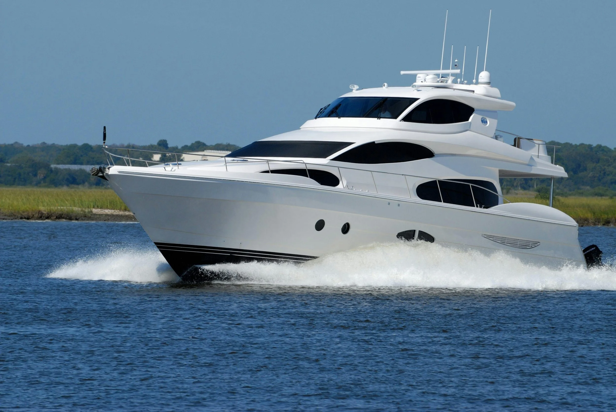 A large white yacht cruising on water with a distant shoreline in the background.