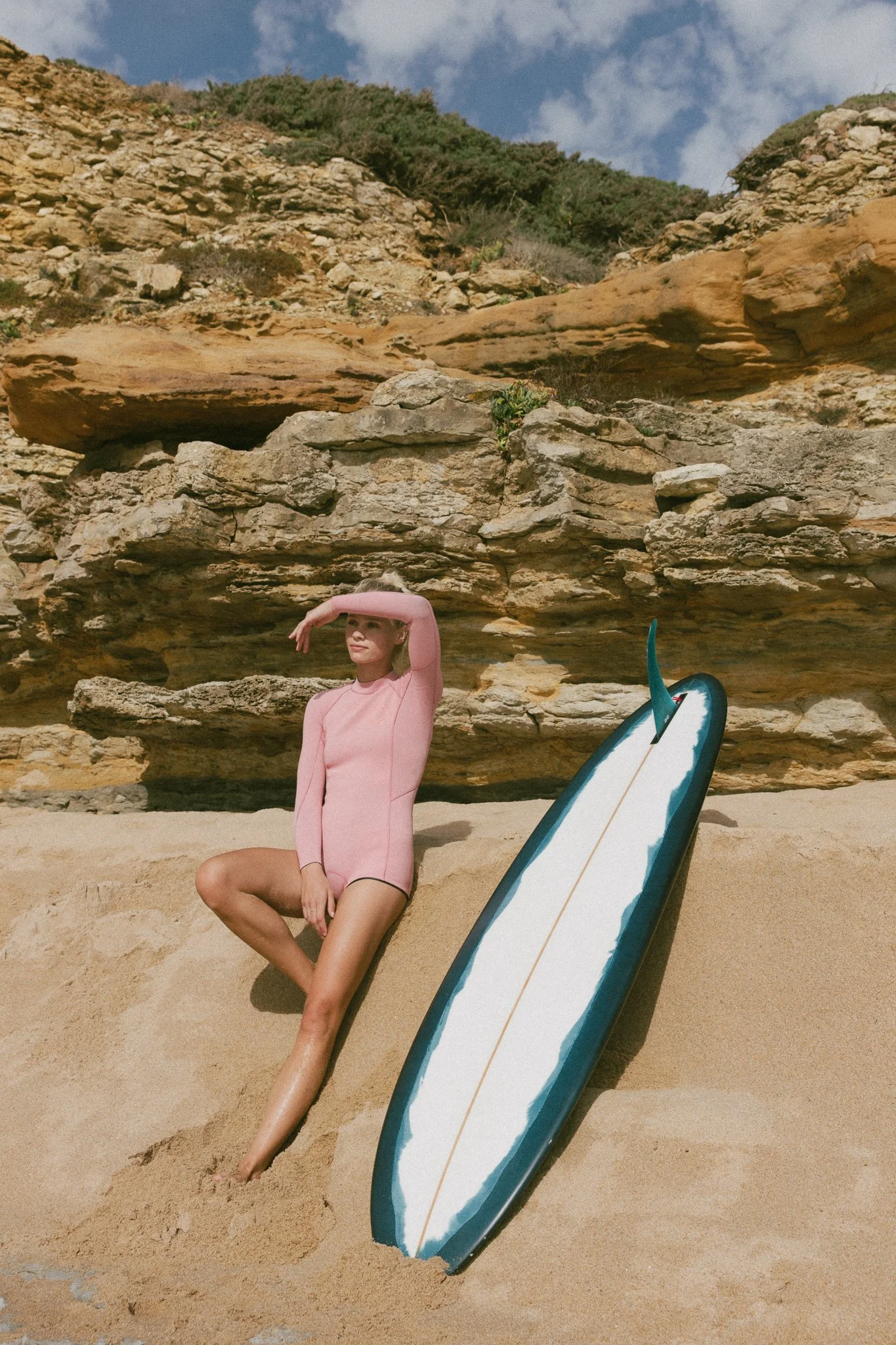 billabong surf suit with model sitting on sand next to surf board