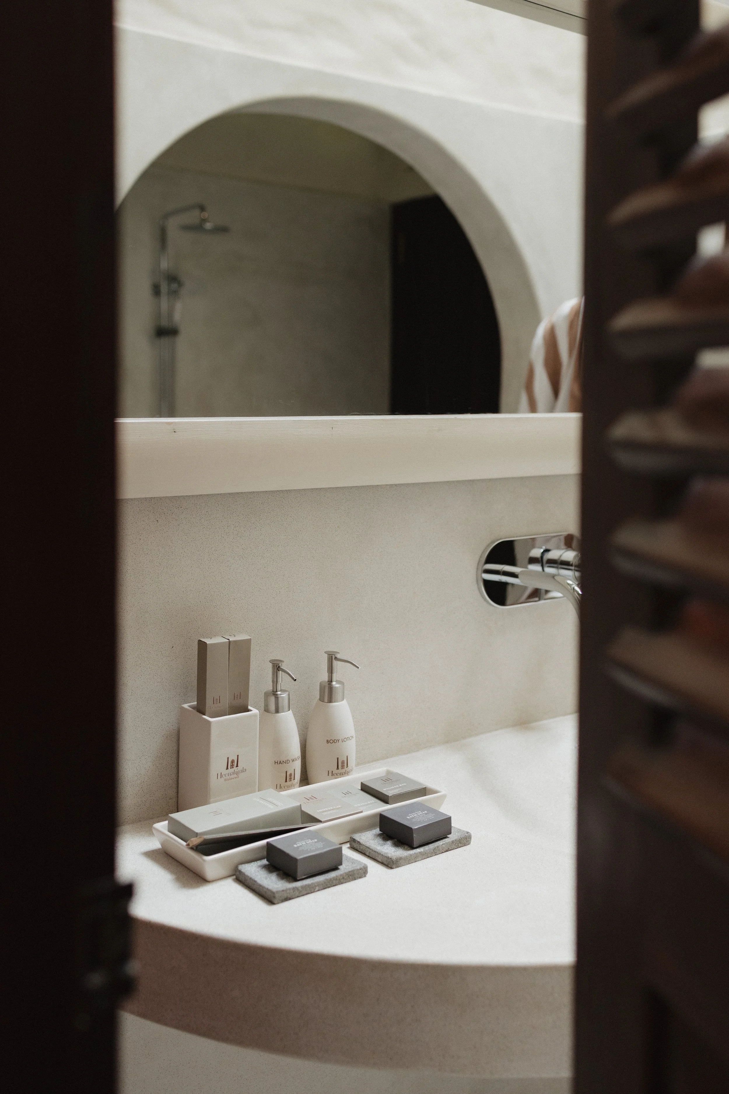 A bathroom sink area with toiletries including hand wash, body lotion, and soap, seen through partially closed wooden shutters at a luxury resort in Sri Lanka