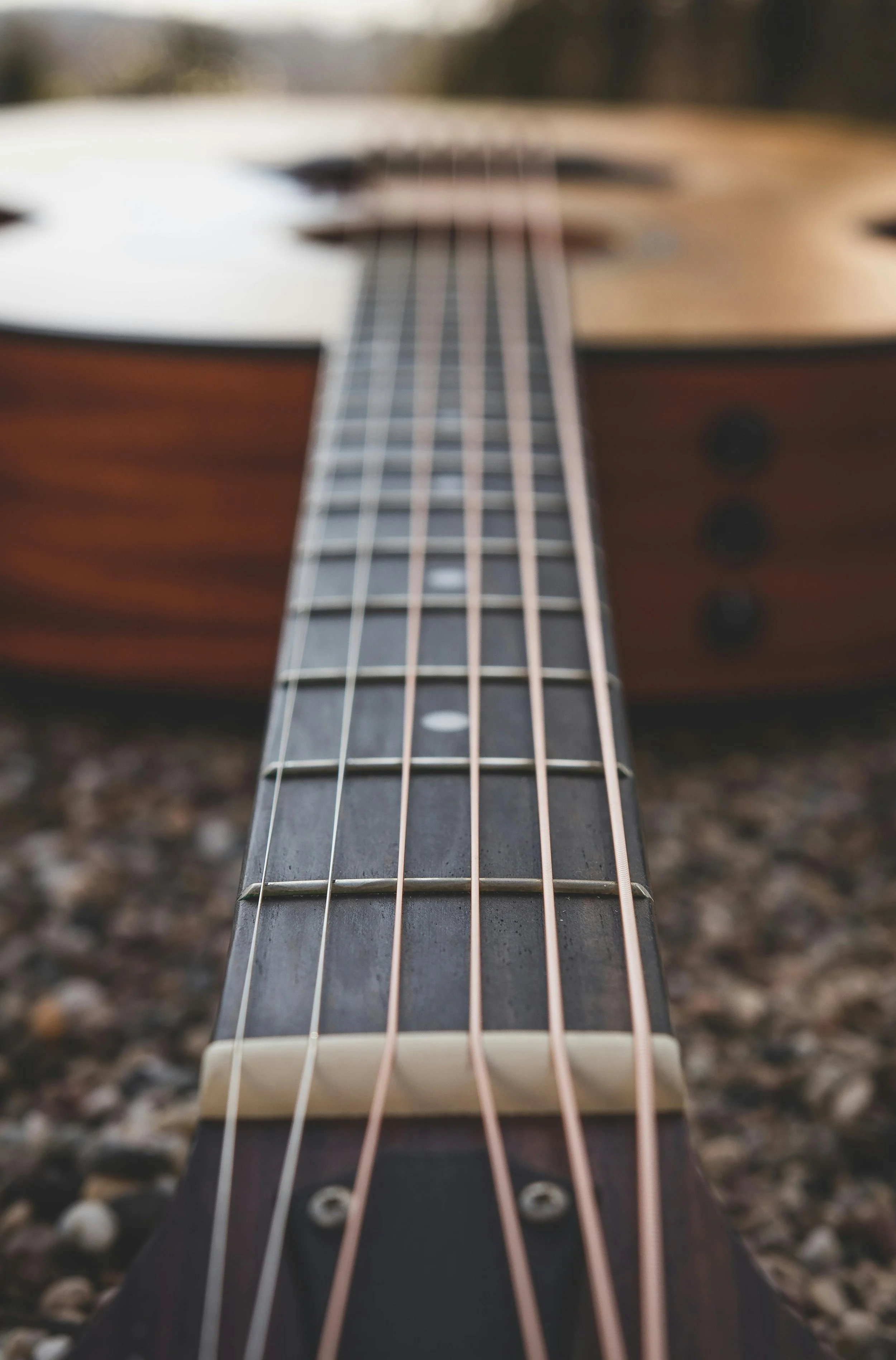 Close-up view of an acoustic guitar neck and fretboard, with the body of the guitar blurred in the background.