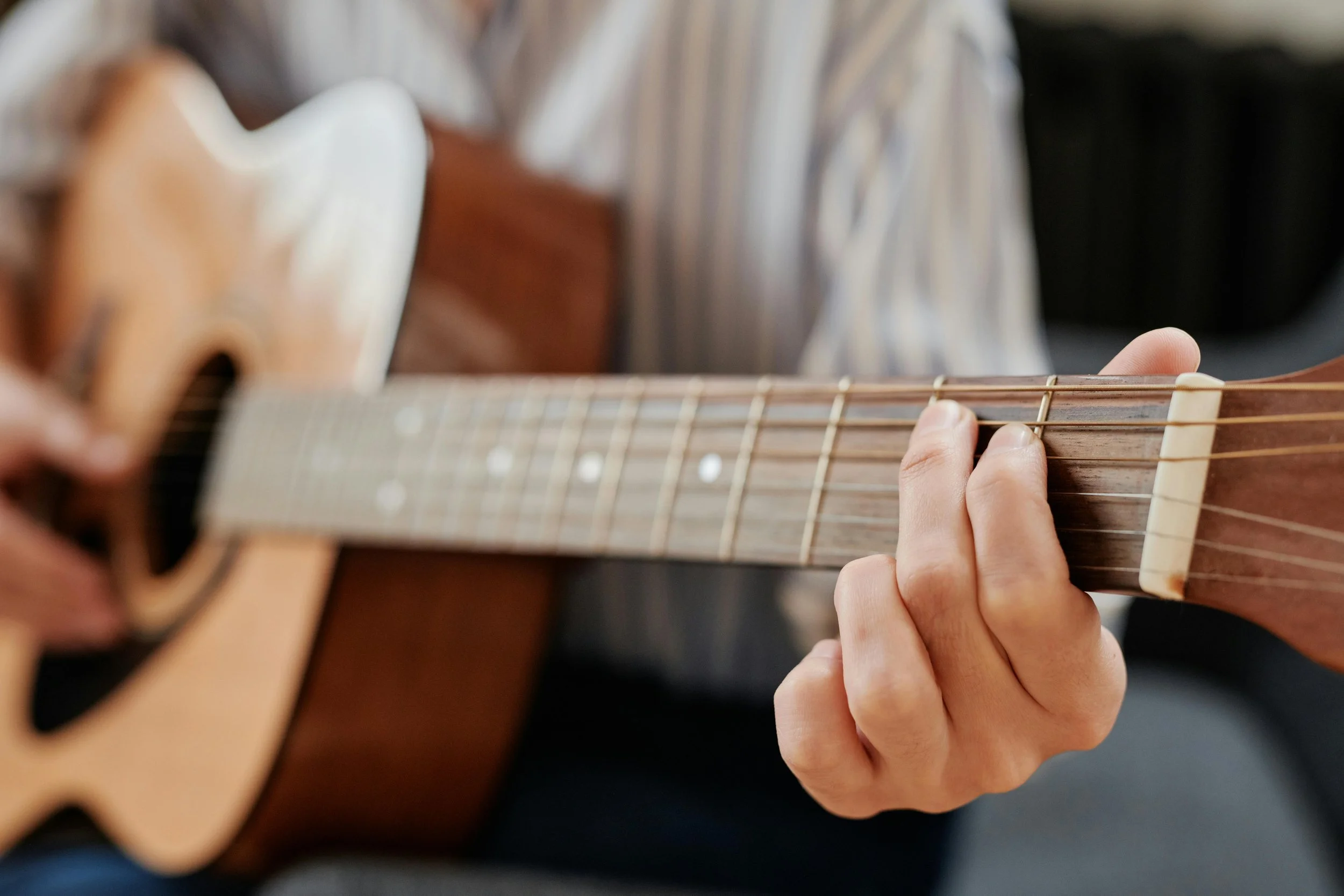 Close-up of a person playing an acoustic guitar, focusing on their hand pressing down on the strings near the fretboard.