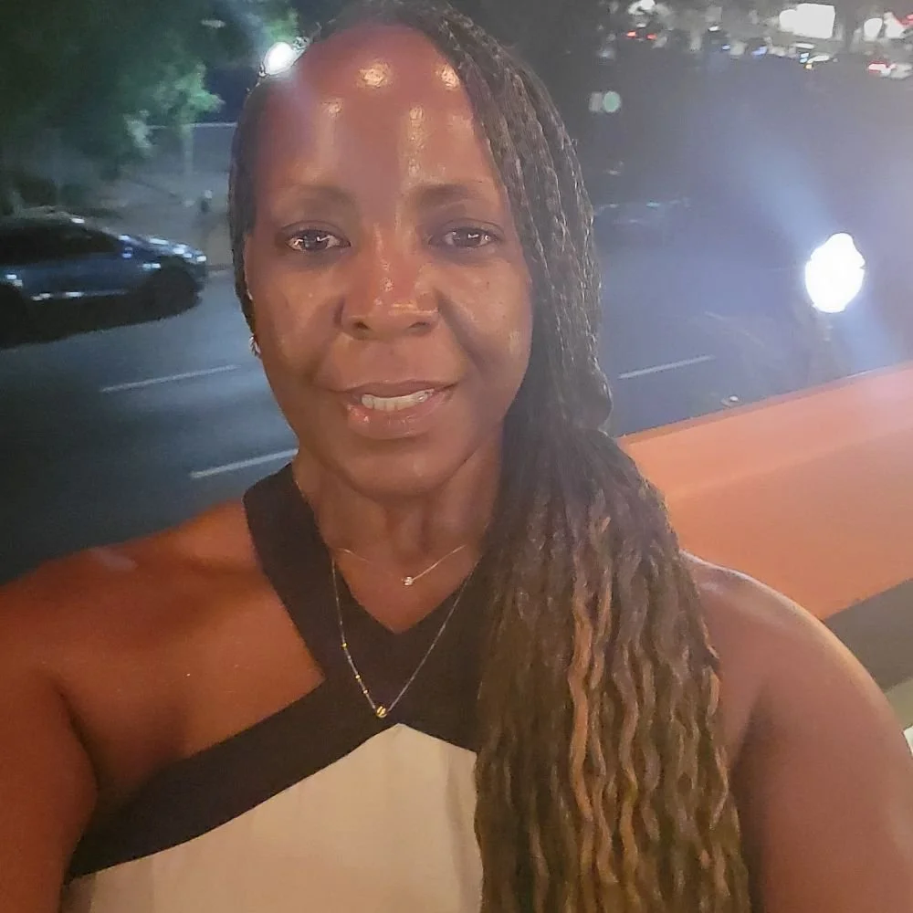 A woman with long, braided hair smiling and taking a selfie at night with a background of a parking lot and cars