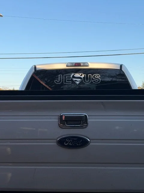 Back of a truck with a sticker that says 'JESUS' with a Superman logo replacing the 'U'.