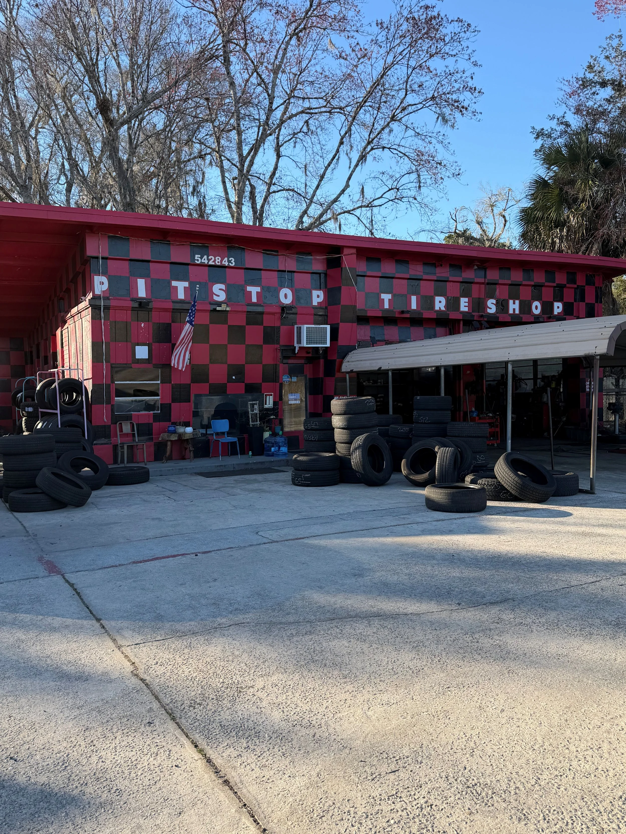 Exterior of Pit Stop Tire Shop with scattered tires and tools, and a pink and black checkered patterned facade.