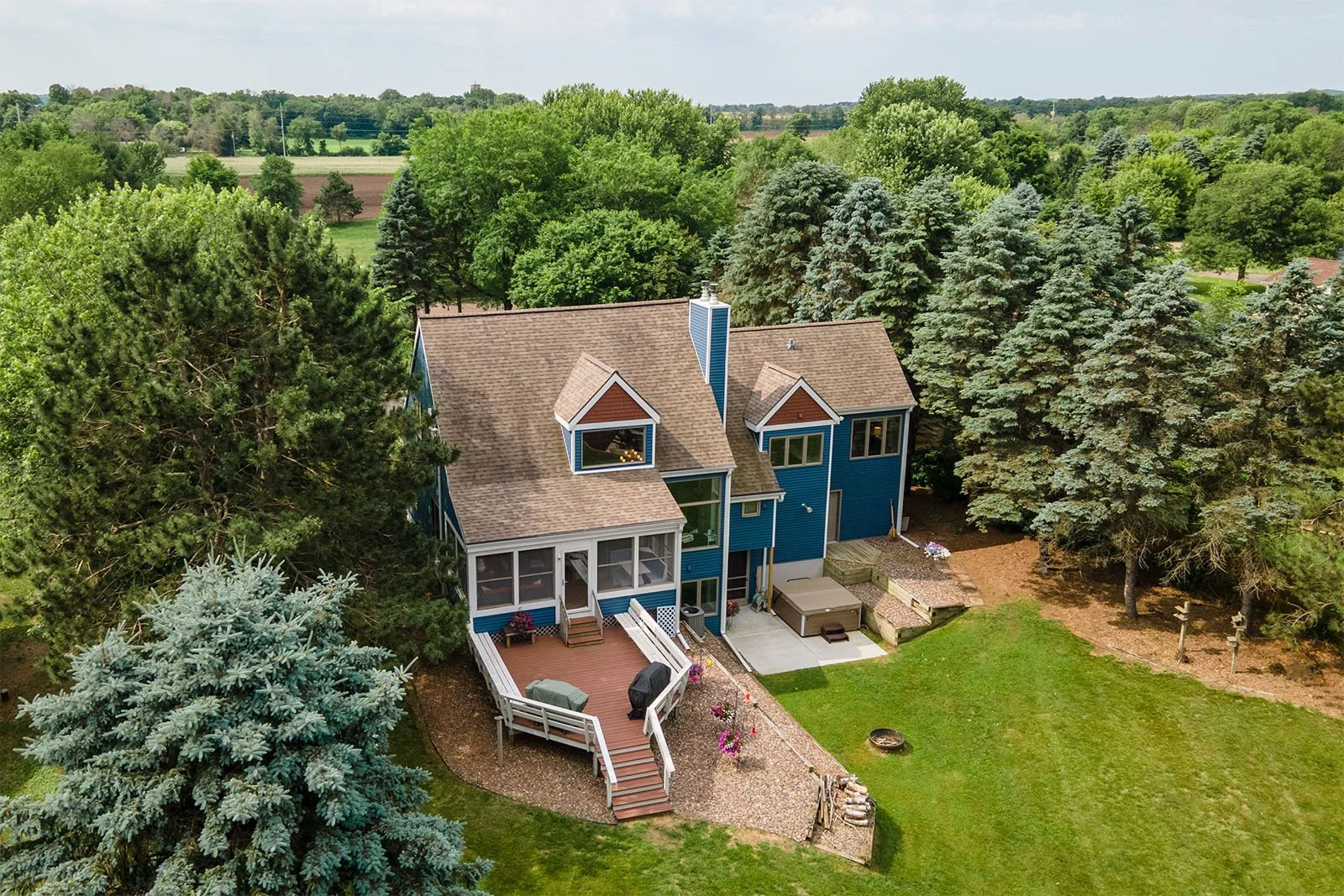 Aerial view of a blue house with a brown roof surrounded by green trees and a grassy yard.