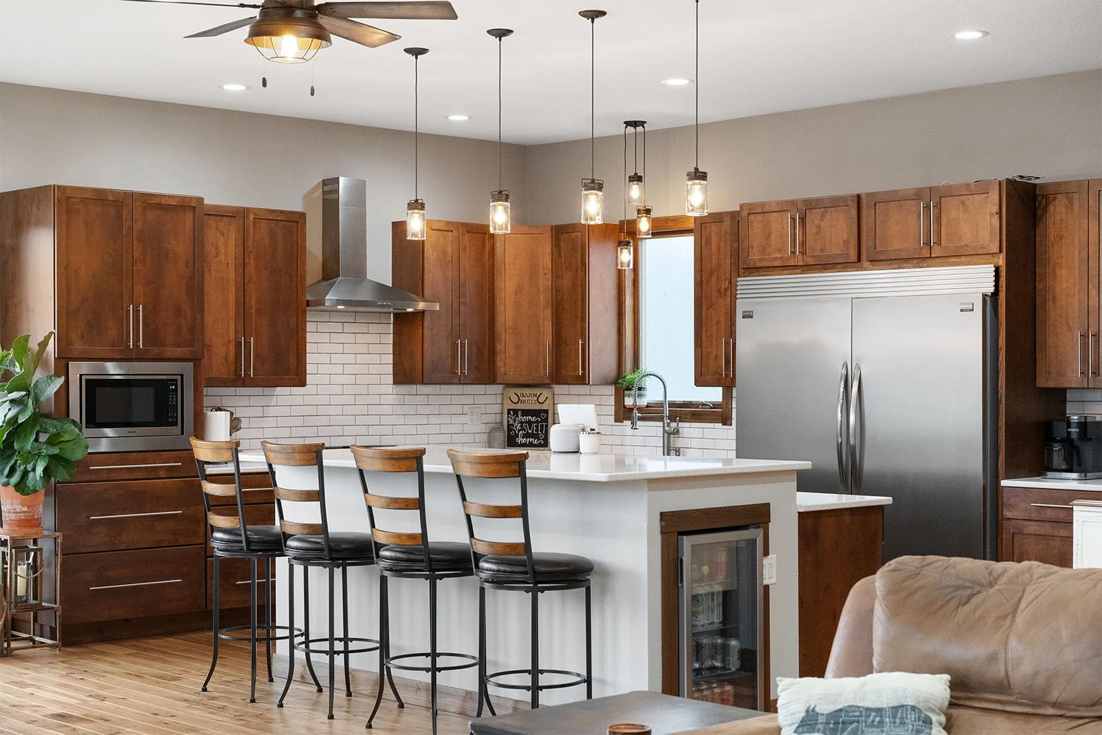 Modern kitchen with wooden cabinets, stainless steel appliances, a white island with bar stools, pendant lights, and a ceiling fan.