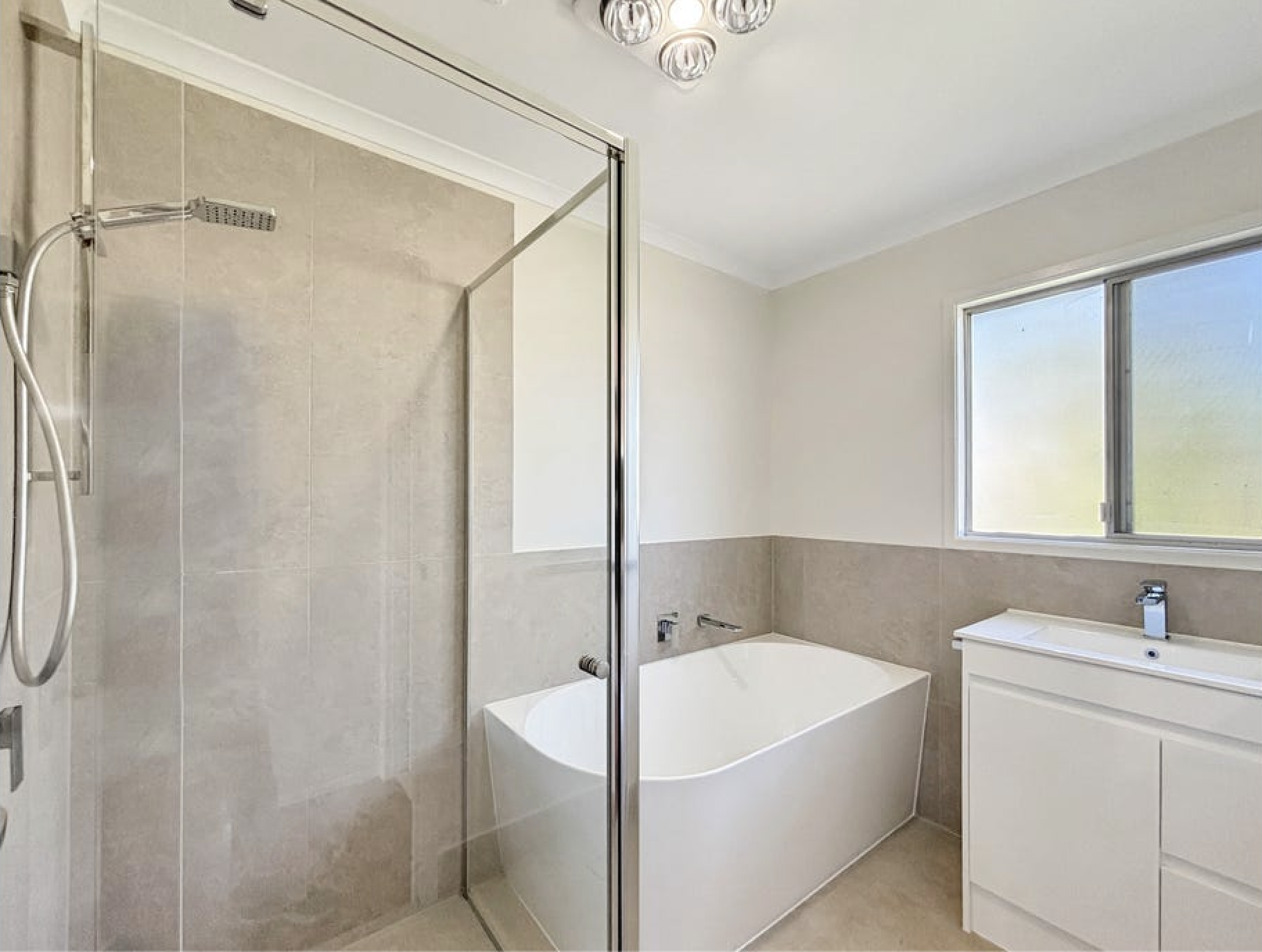 Modern bathroom with a walk-in glass shower, a bathtub, a window, and white cabinetry.