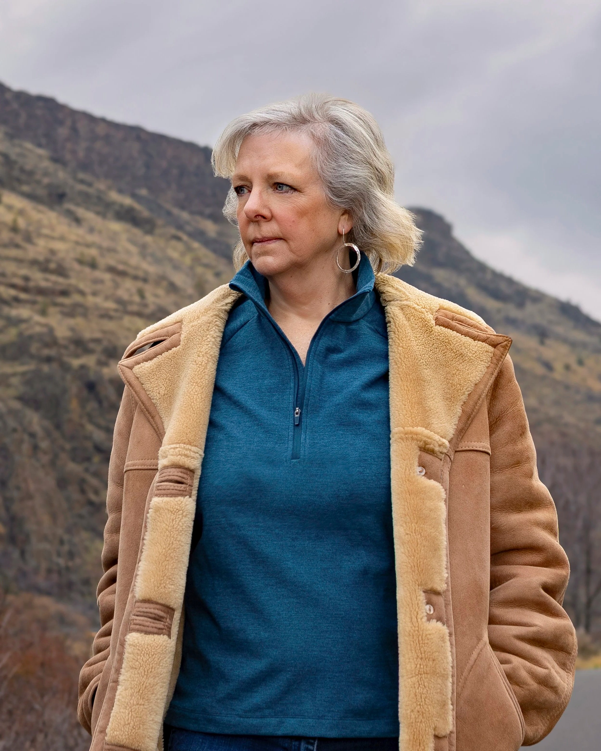 Lisa Gambee A woman with blonde hair wearing a brown shearling coat and a blue zip-up jacket standing outdoors with mountainous terrain in the background. - Vote wasco county commissioner The Dalles South Wasco County Tygh Valley Maupin Dufur