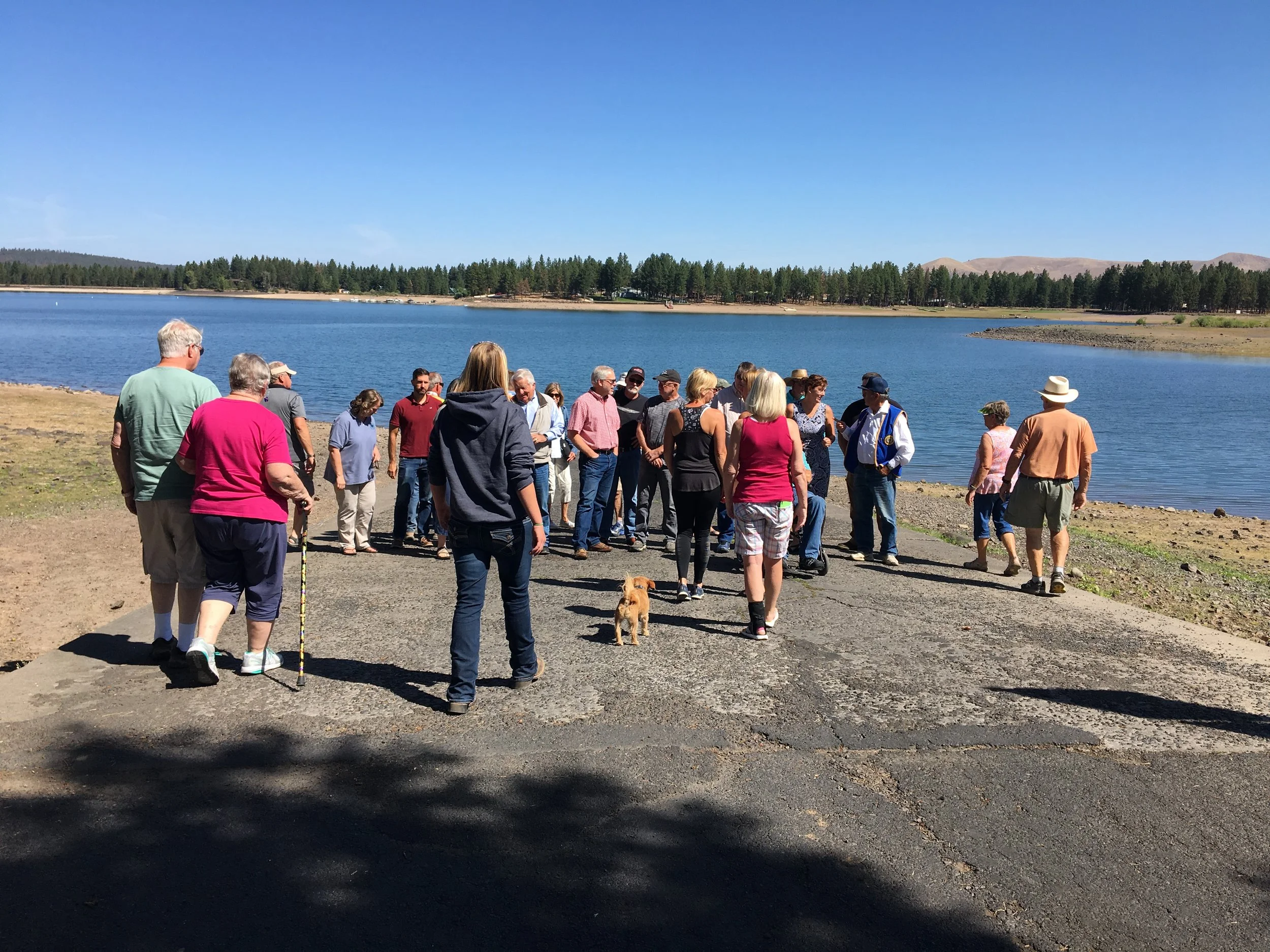 Group of people gathered on pine creek boat ramp on a sunny day, with trees and hills in the background. South Wasco County