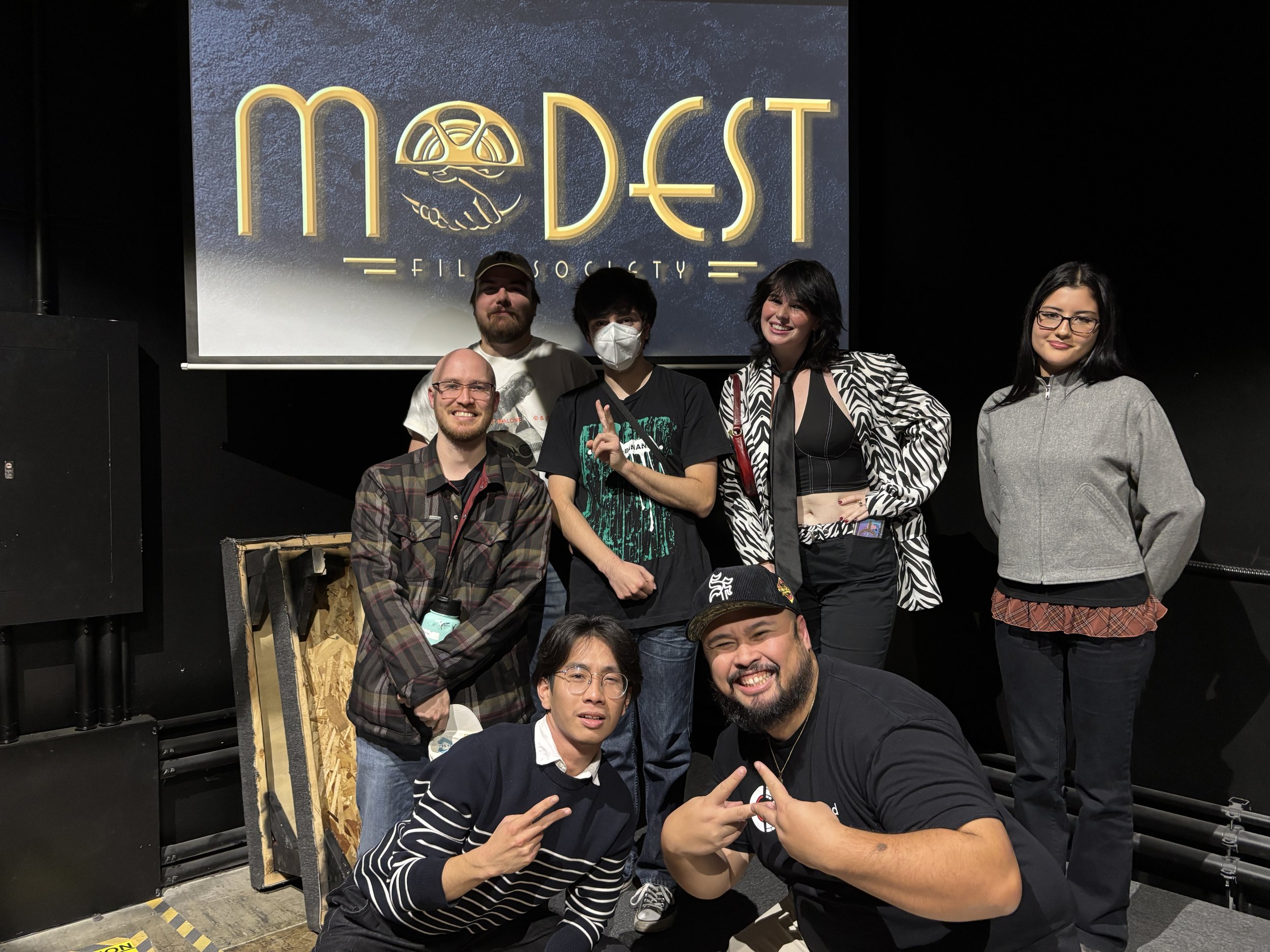 Group of filmmakers posing together on stage in front of a Modest Film Society projection screen after a screening event.