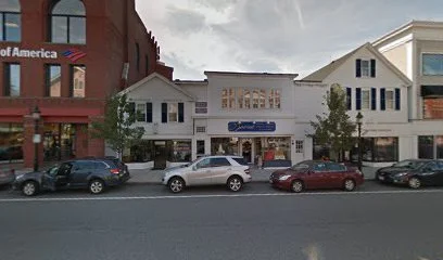A downtown street scene with a white building labeled 'The Historic' in the center, cars parked along the curb, and trees on either side. To the left, part of a building with a sign reading 'of America' is visible.