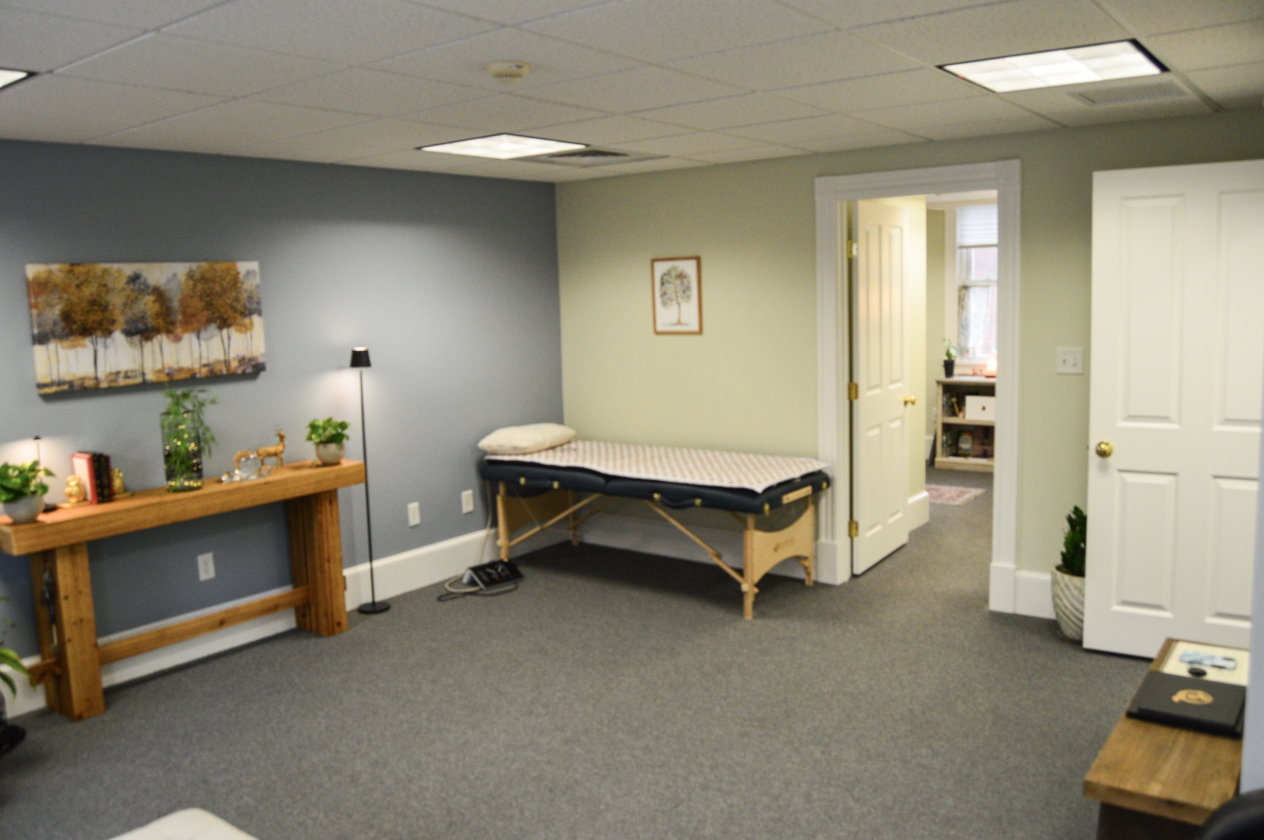 A person holding a singing bowl with one hand and a mallet with the other, surrounded by crystals and a smudging bundle on a textured surface.