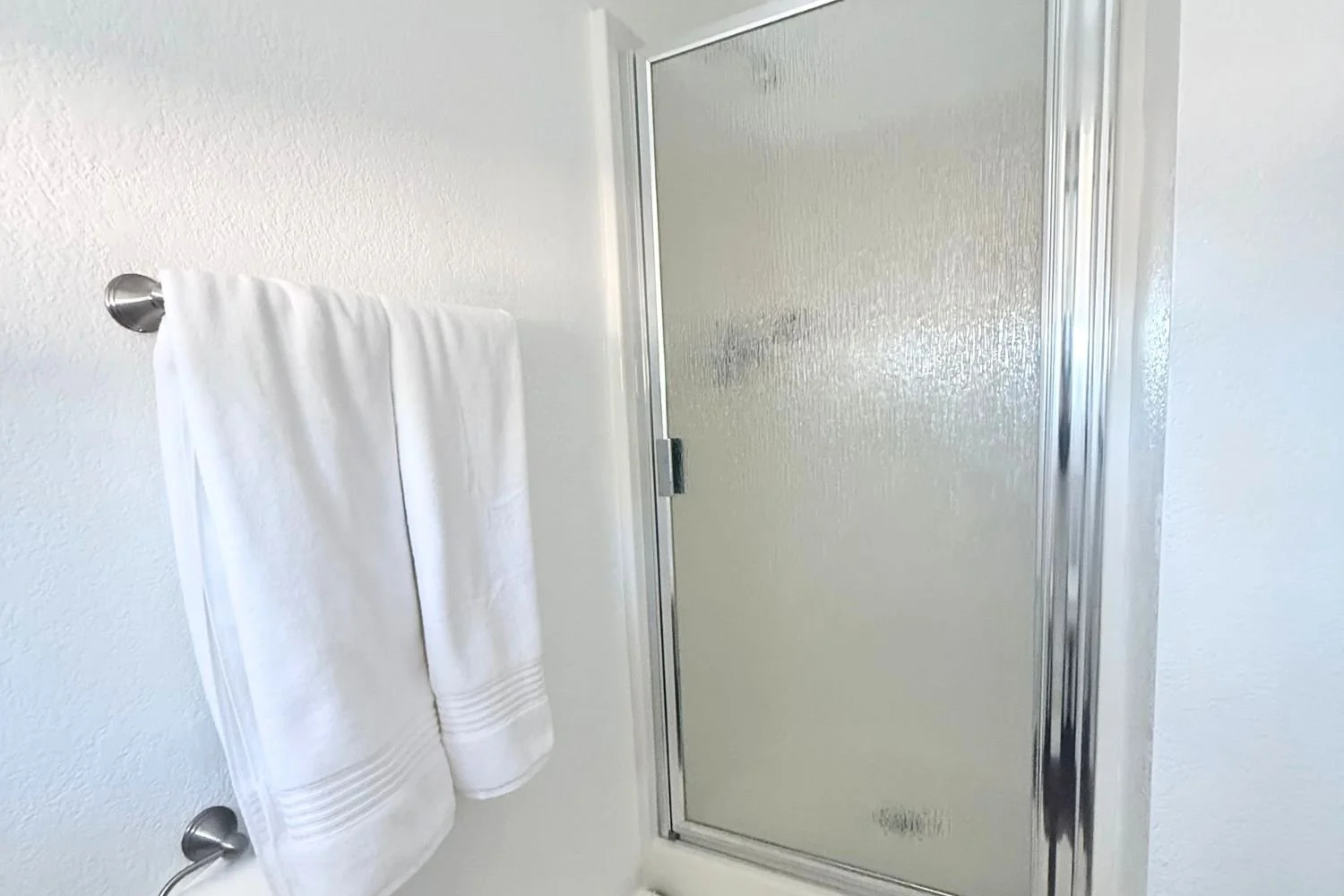 Bathroom shower with textured glass door, white towel hanging on a metal towel rod on a white wall.