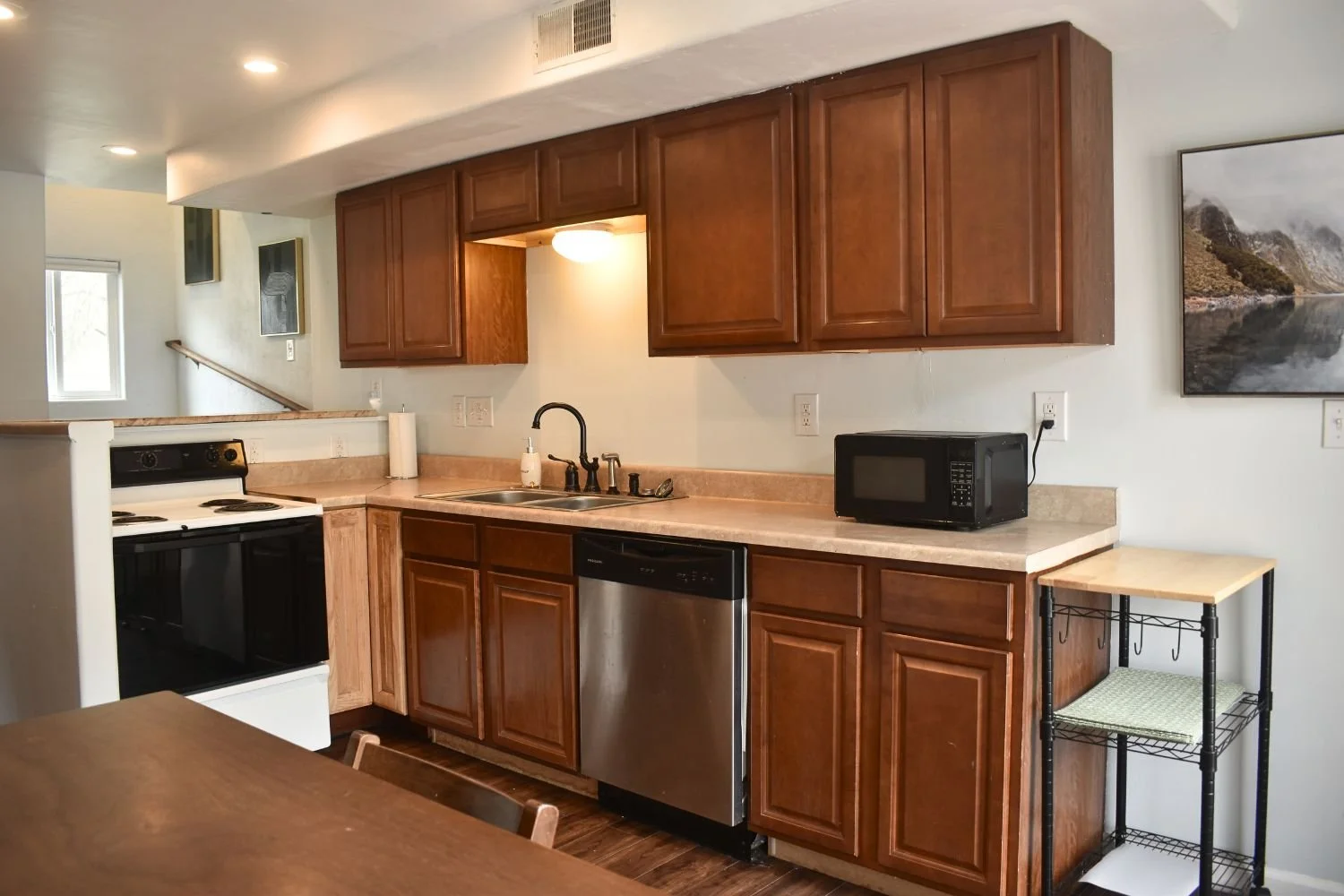 Kitchen with wooden cabinets, a black stove, a sink with a black faucet, a stainless steel dishwasher, a microwave, and small shelving unit.