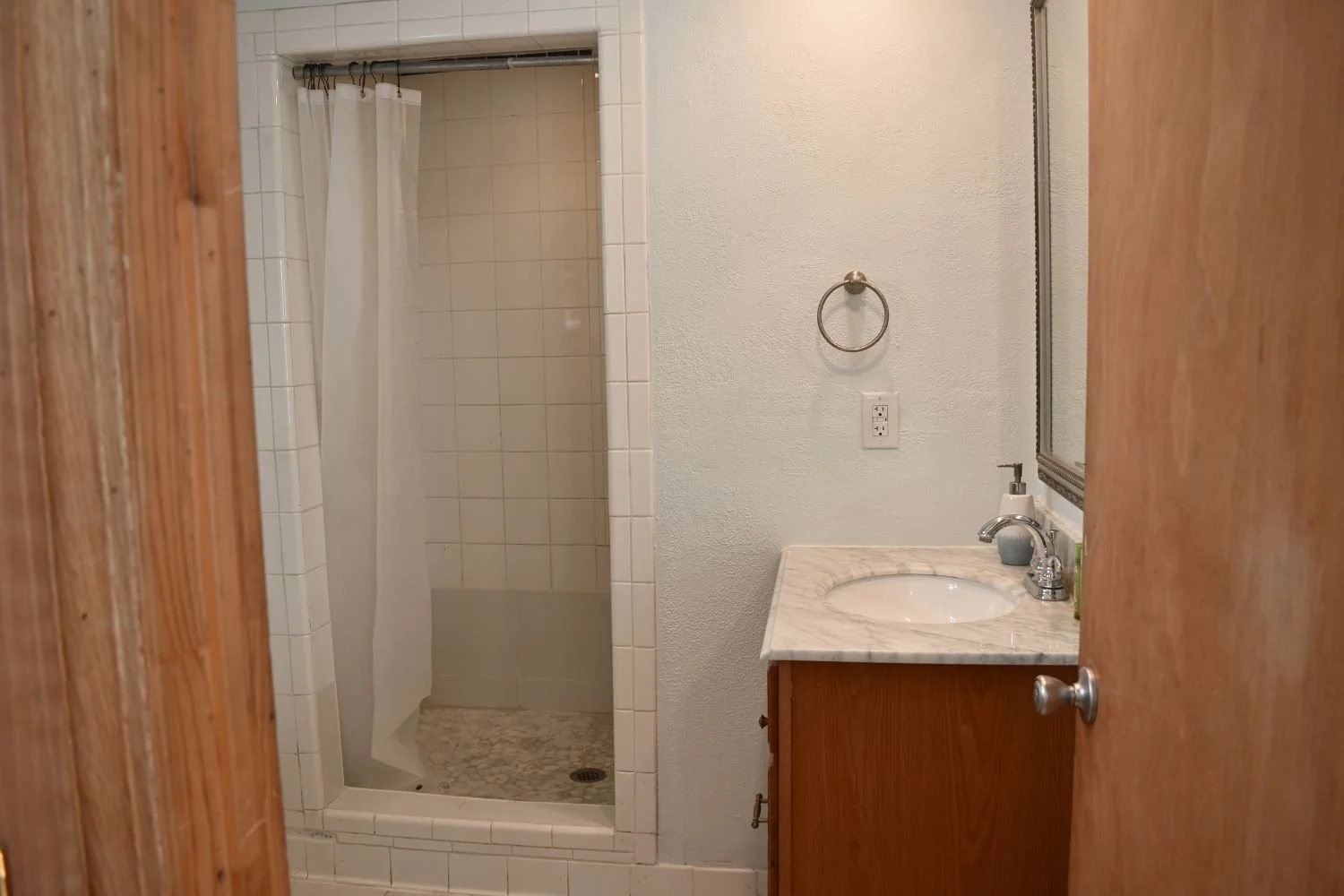 Bathroom with a shower, white tile walls, and a small vanity with a marble countertop and faucet.