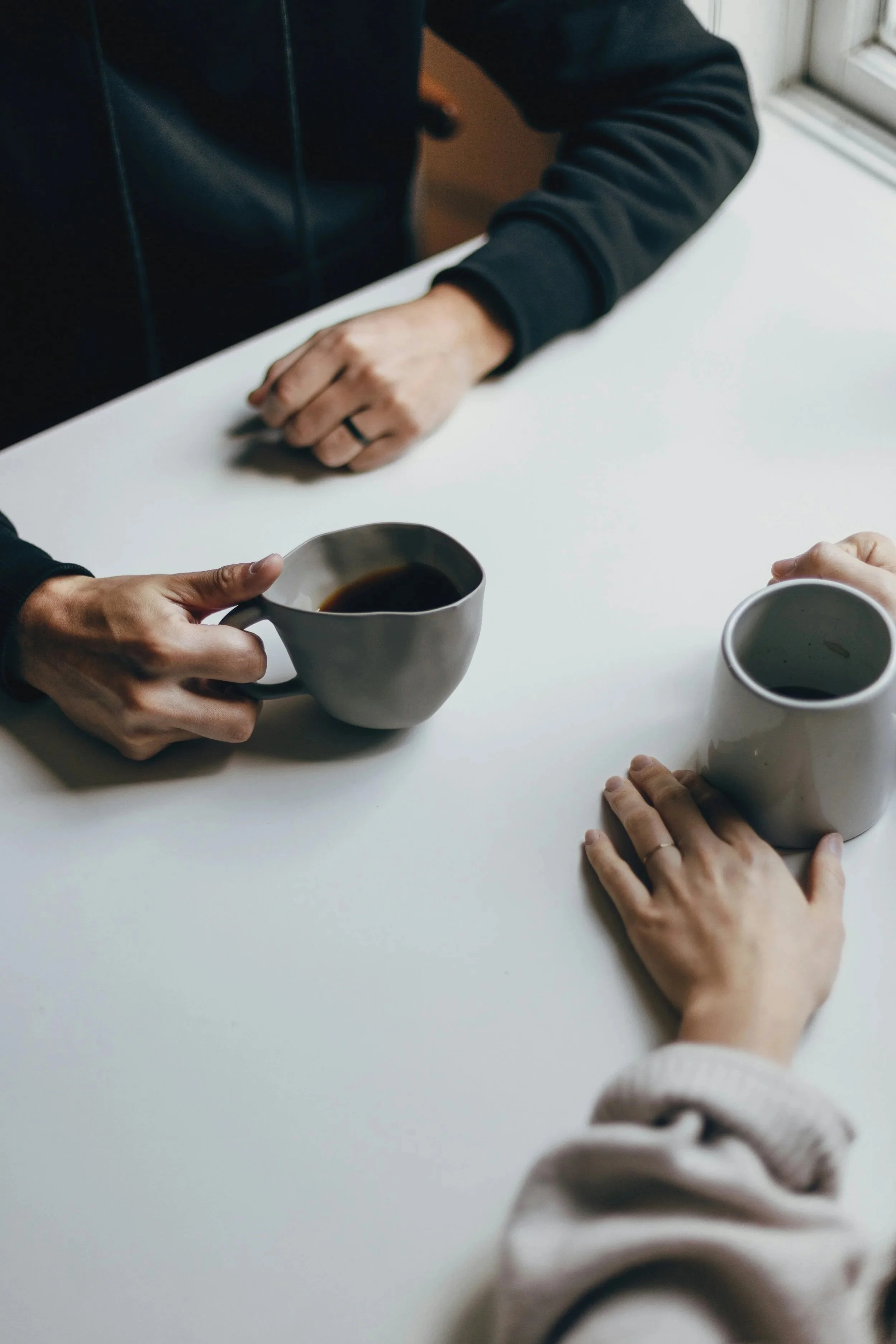 Two adults sitting across a table in conversation with coffee mugs