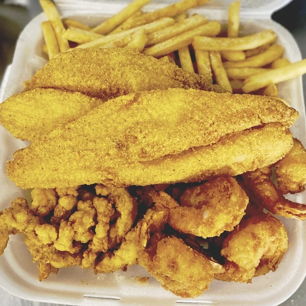 Fried fish fillets with French fries and fried chicken pieces in a foam takeout container.