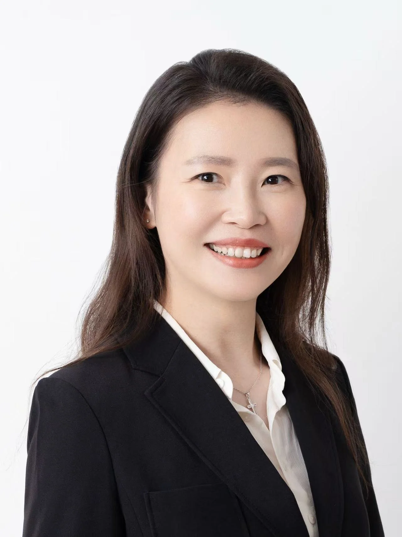 Professional portrait of a woman with long dark hair wearing a black blazer and white shirt, smiling at the camera against a plain white background.