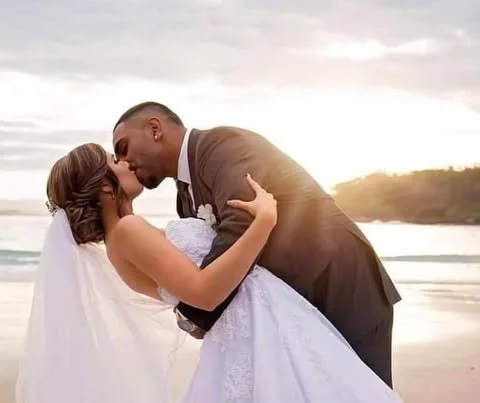 A newlywed couple on the beach at sunset, embracing affectionately.