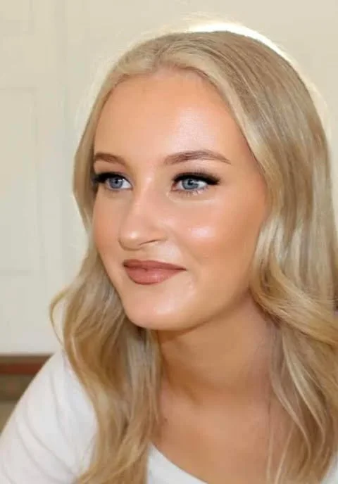 A woman with long blonde hair, blue eyes, and a slight smile, looking to the side.