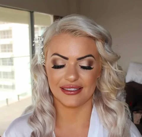 Close-up of a woman with platinum blonde wavy hair, makeup, and a decorative hair clip.