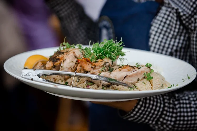 A plate of grilled chicken served with couscous, microgreens, and a lemon wedge.