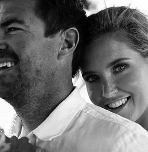A man and woman smiling, with the woman leaning on the man's shoulder.