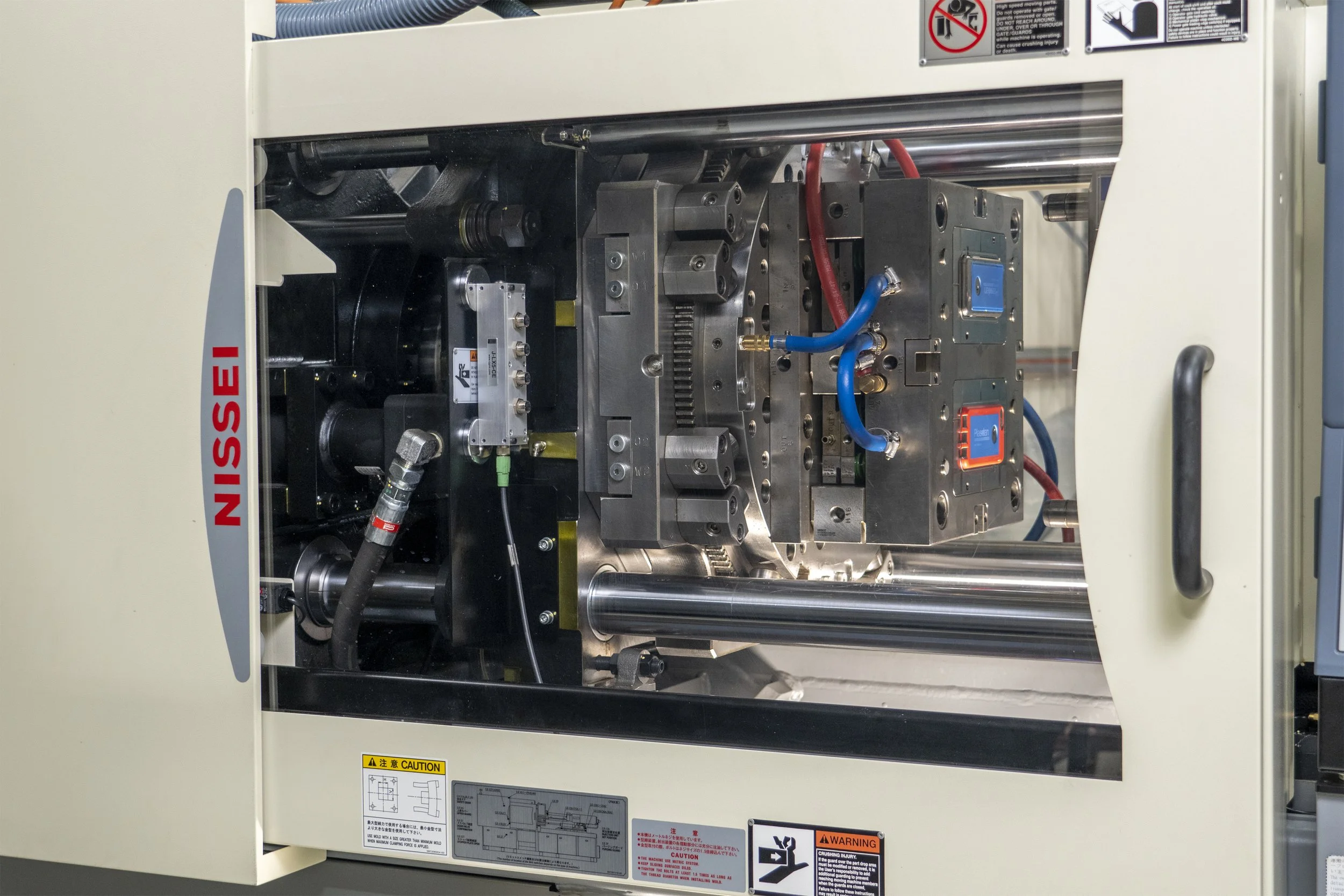 Close-up view of industrial machinery inside a beige metal cabinet with warning labels, metal components, wiring, and hydraulic tubes.