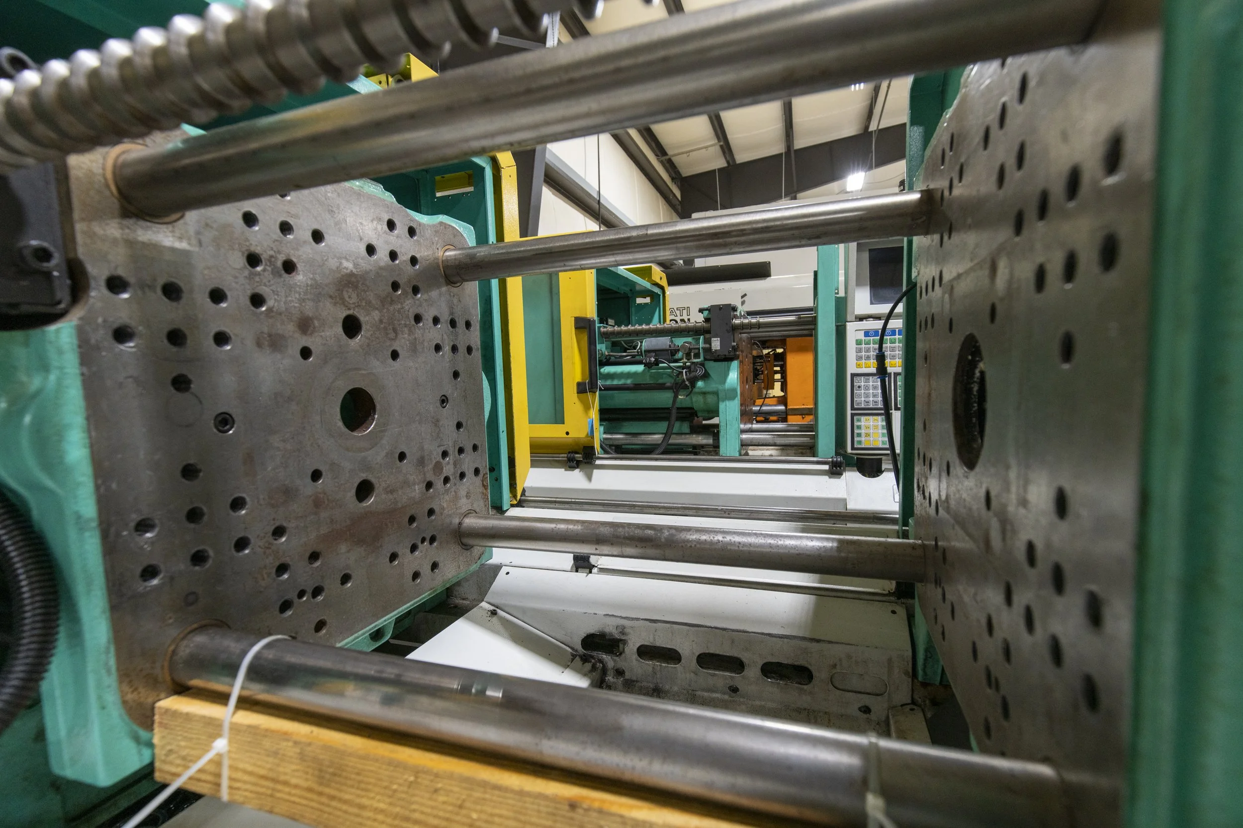 Close-up of industrial machinery parts including metal rods, perforated metal plates, and electronic control panels in a factory setting.