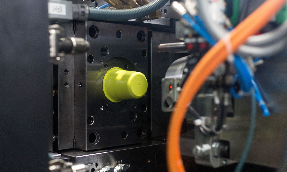 Close-up of a mechanical or industrial device featuring a yellow-green plastic component mounted on a metal surface, surrounded by various colored and gray wires and metallic parts.