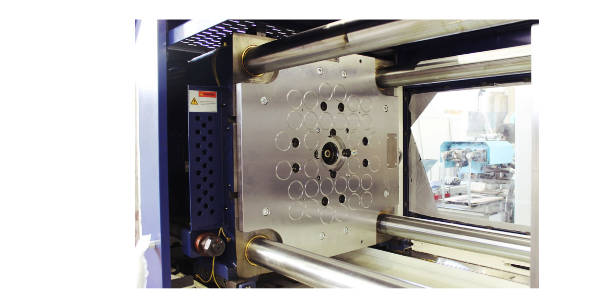 Close-up of industrial machinery with metal components and a perforated metal plate, with some wiring and control parts visible on the side.