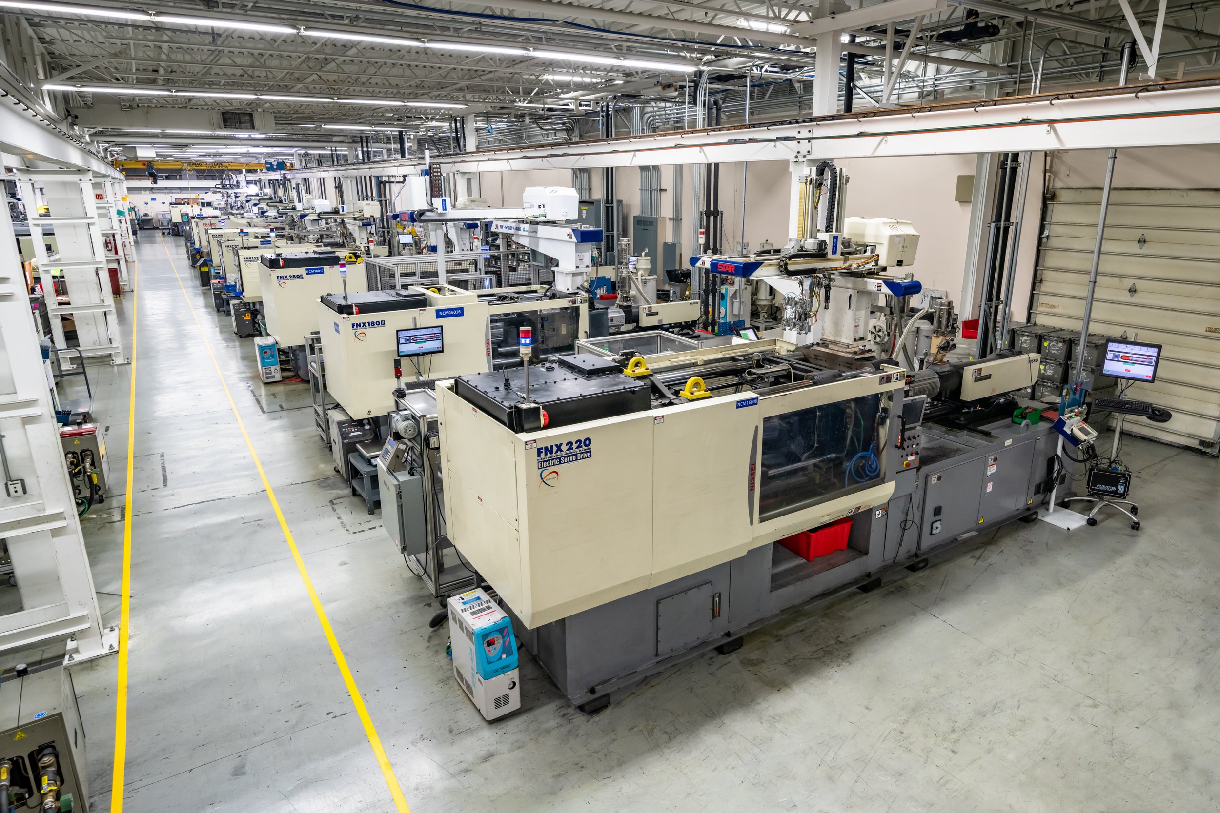Industrial manufacturing facility with multiple large CNC machines arranged in rows within a spacious, well-lit factory