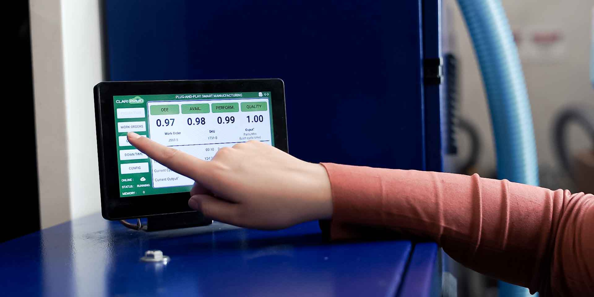 Person using a touchscreen control panel with green and white interface, displaying metrics like OEE, AVAIL, PERFORM, and QUALITY, in an industrial setting.