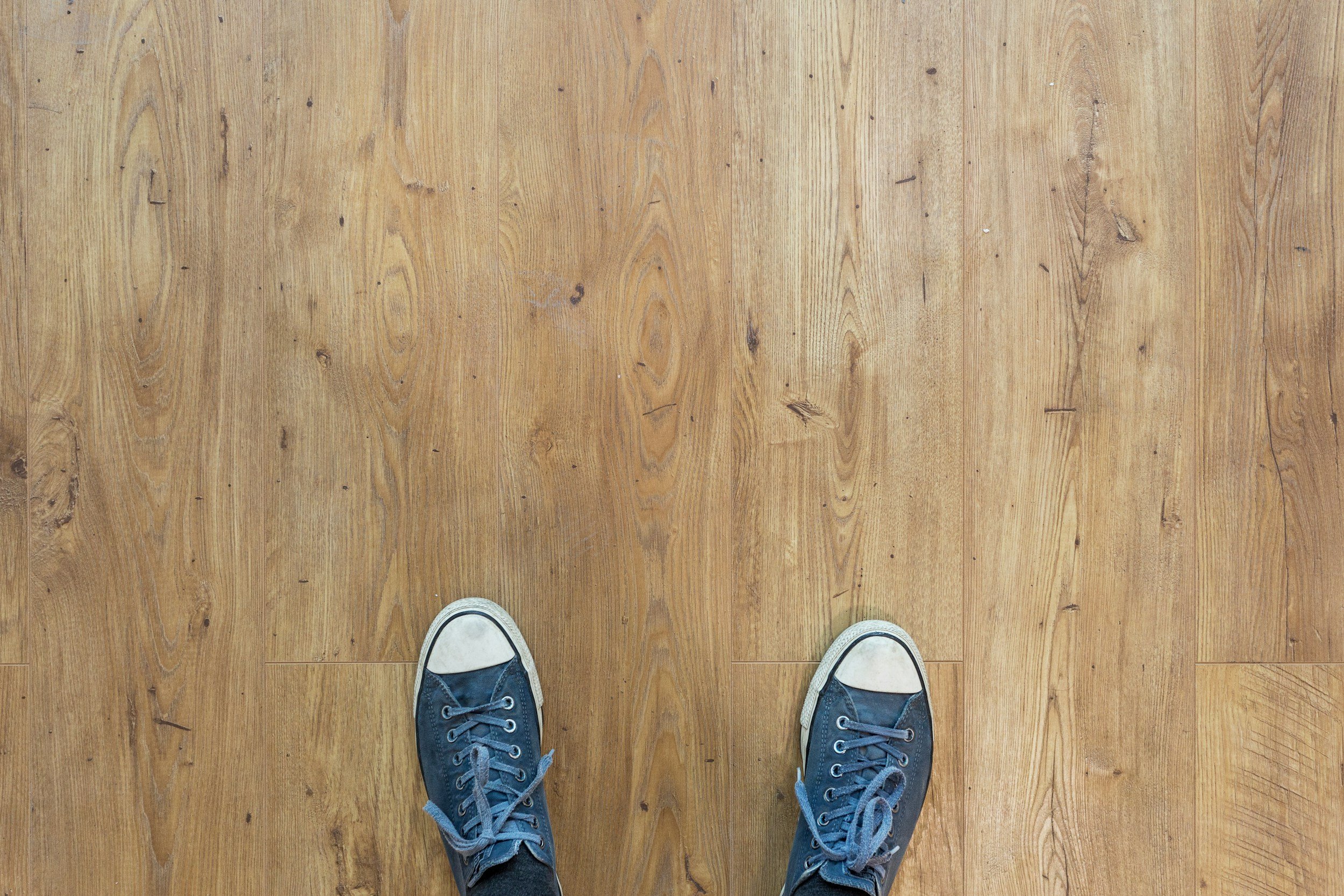 Top-down view of person wearing blue sneakers standing on a wooden floor.